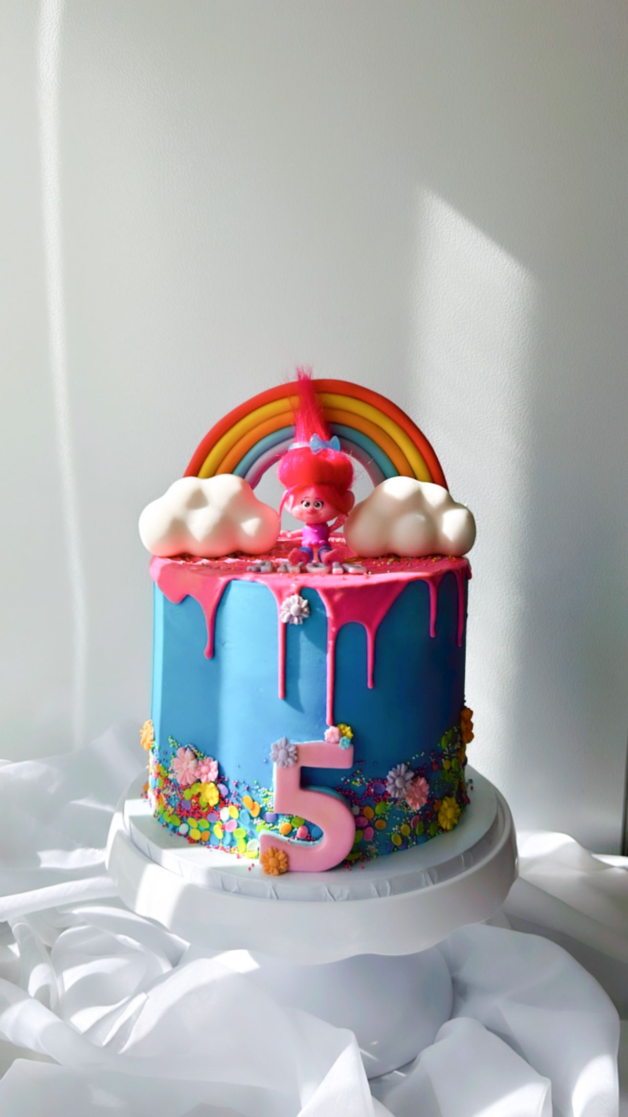 A trolls birthday cake with a rainbow , clouds and a number 5 on top of it.