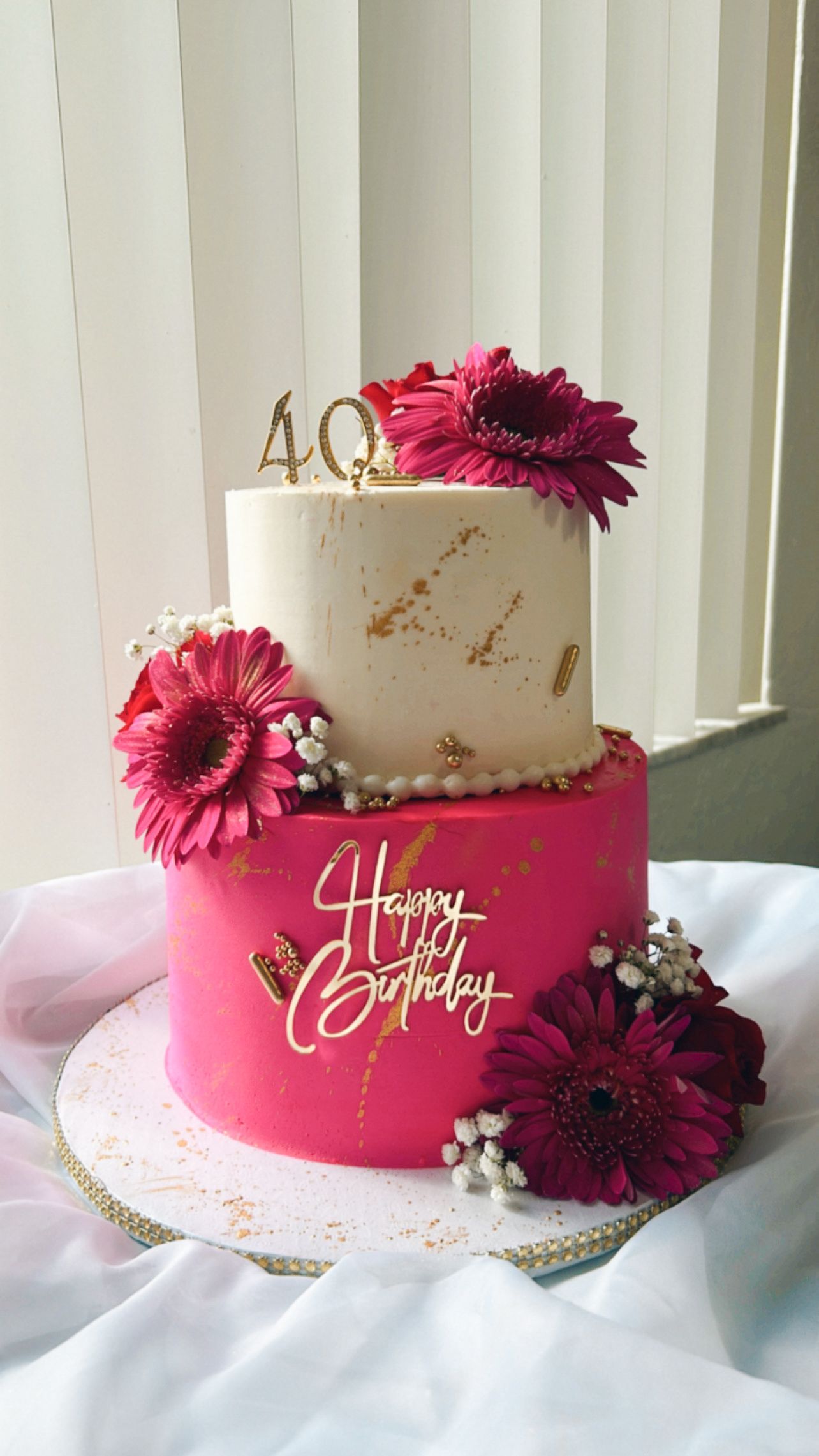 A pink and white birthday cake with flowers on it is sitting on a table.