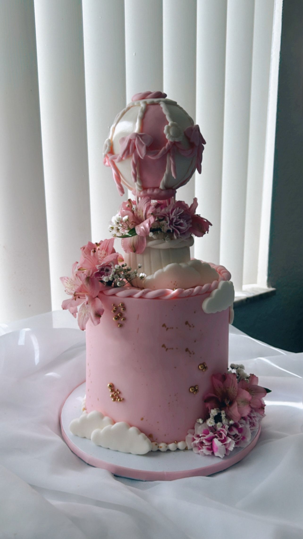 A pink cake with a hot air balloon on top of it is sitting on a table.