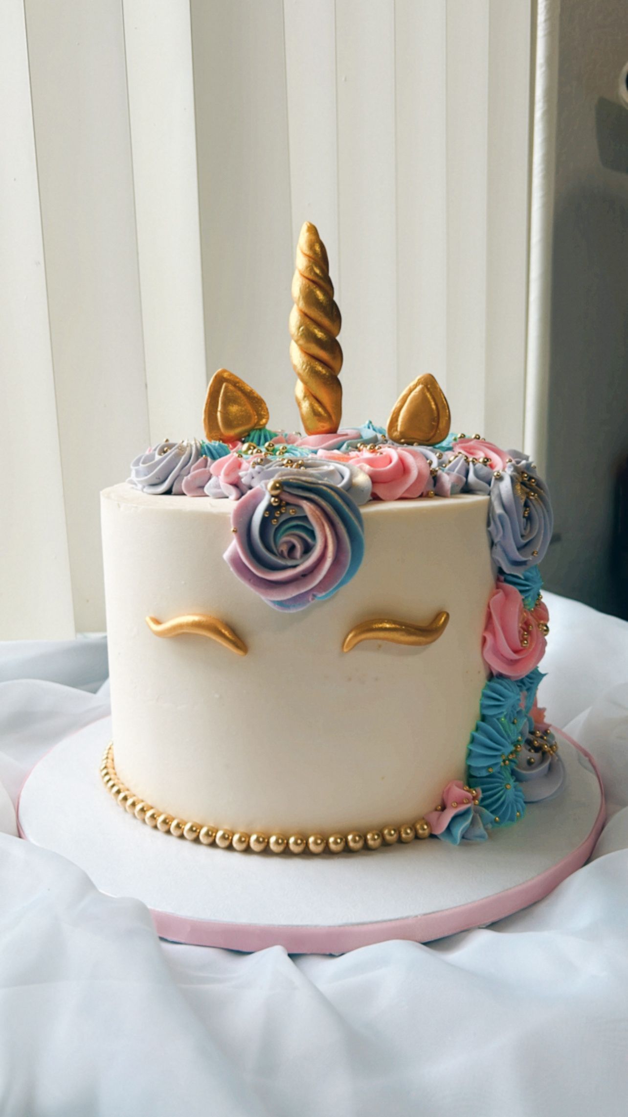 A white cake decorated to look like a unicorn is sitting on a table.