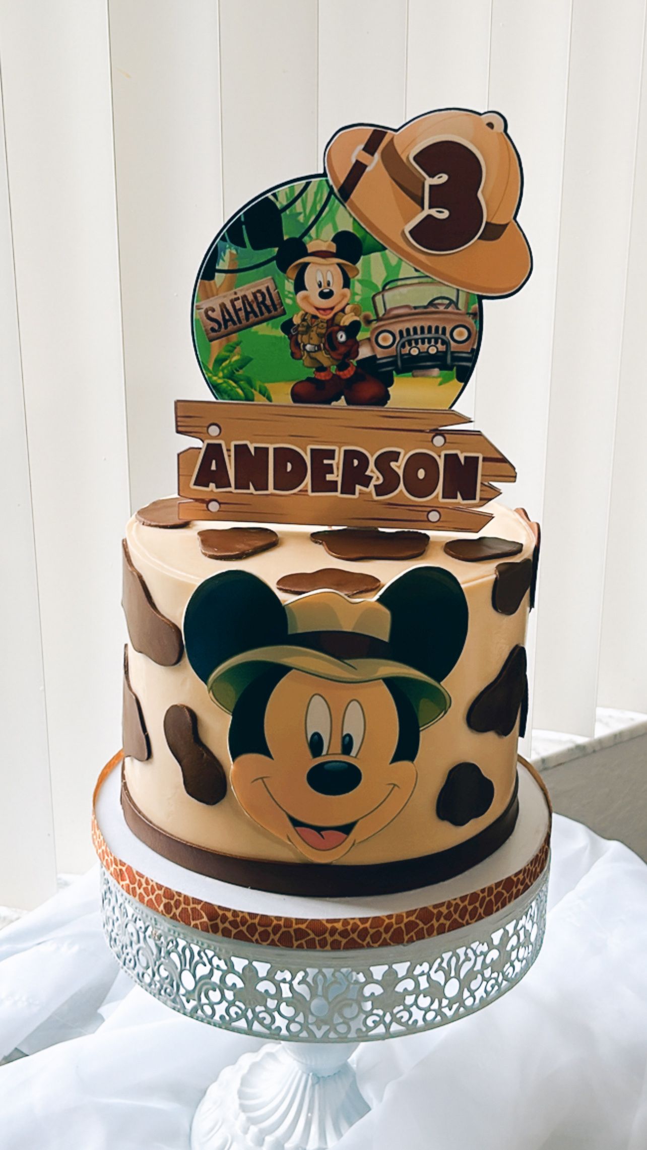 A cake with mickey mouse on it is on a cake stand on a table.