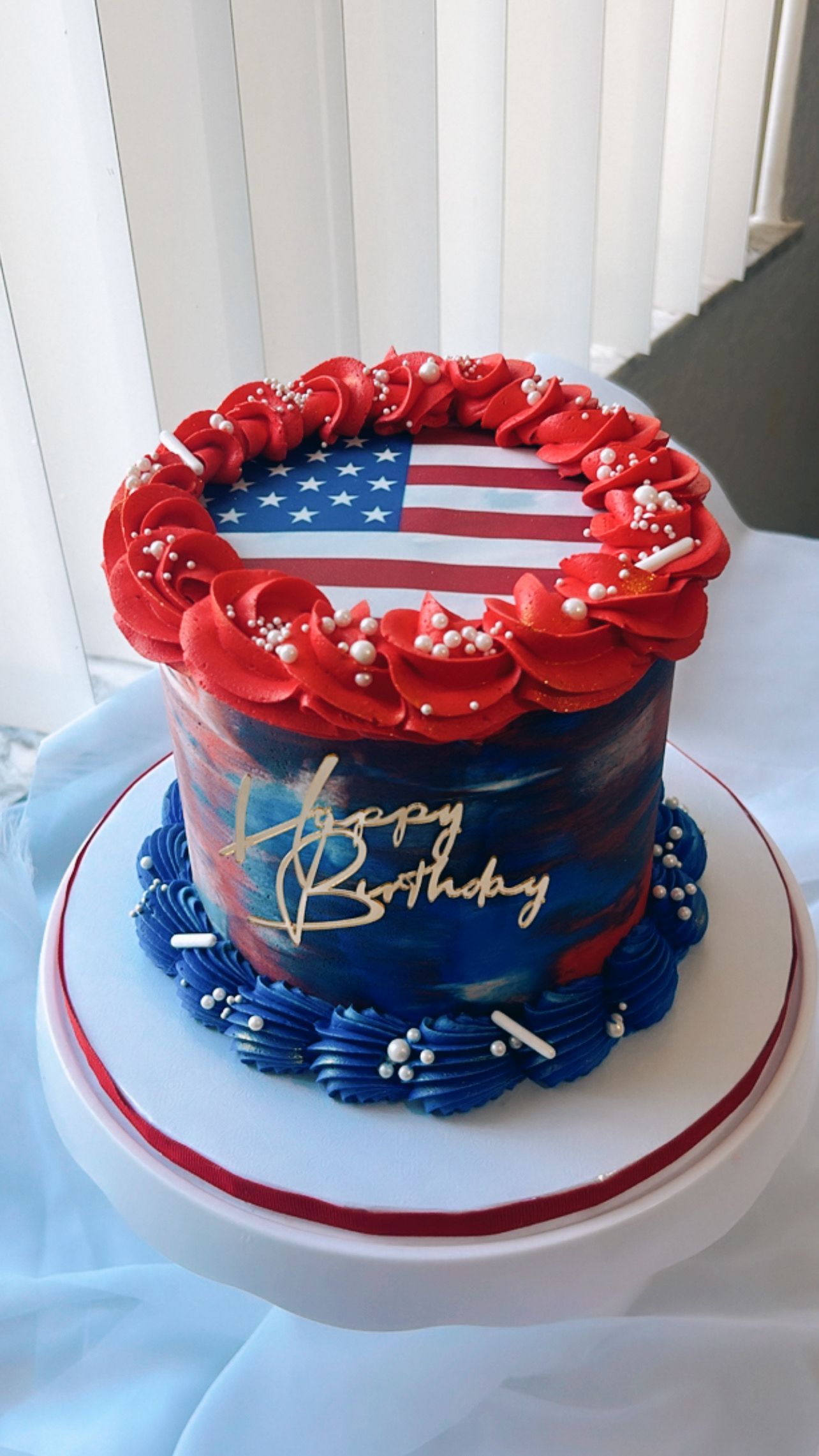 A red , white and blue birthday cake with an american flag on top.