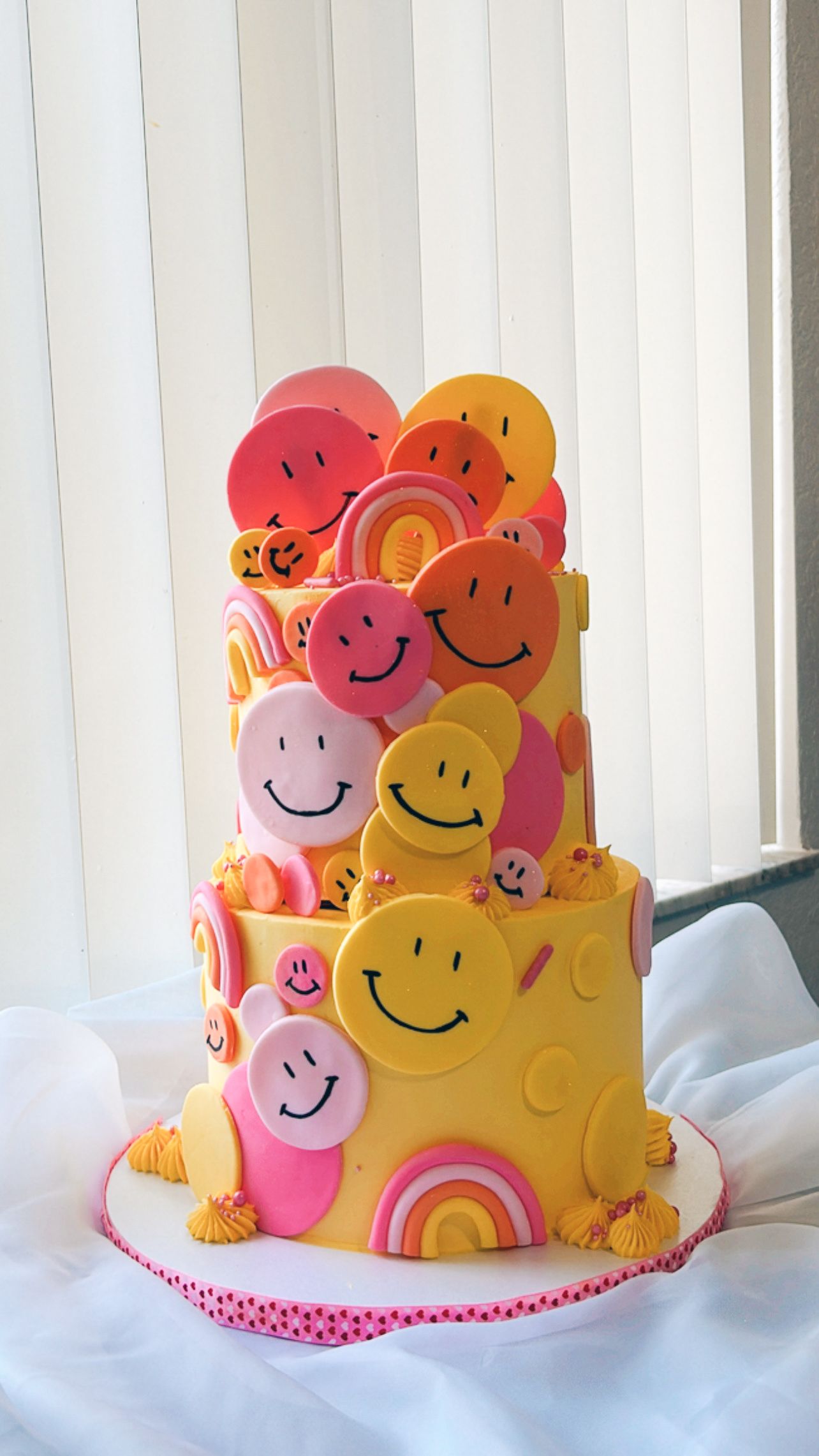 A yellow cake with smiley faces and rainbows on it