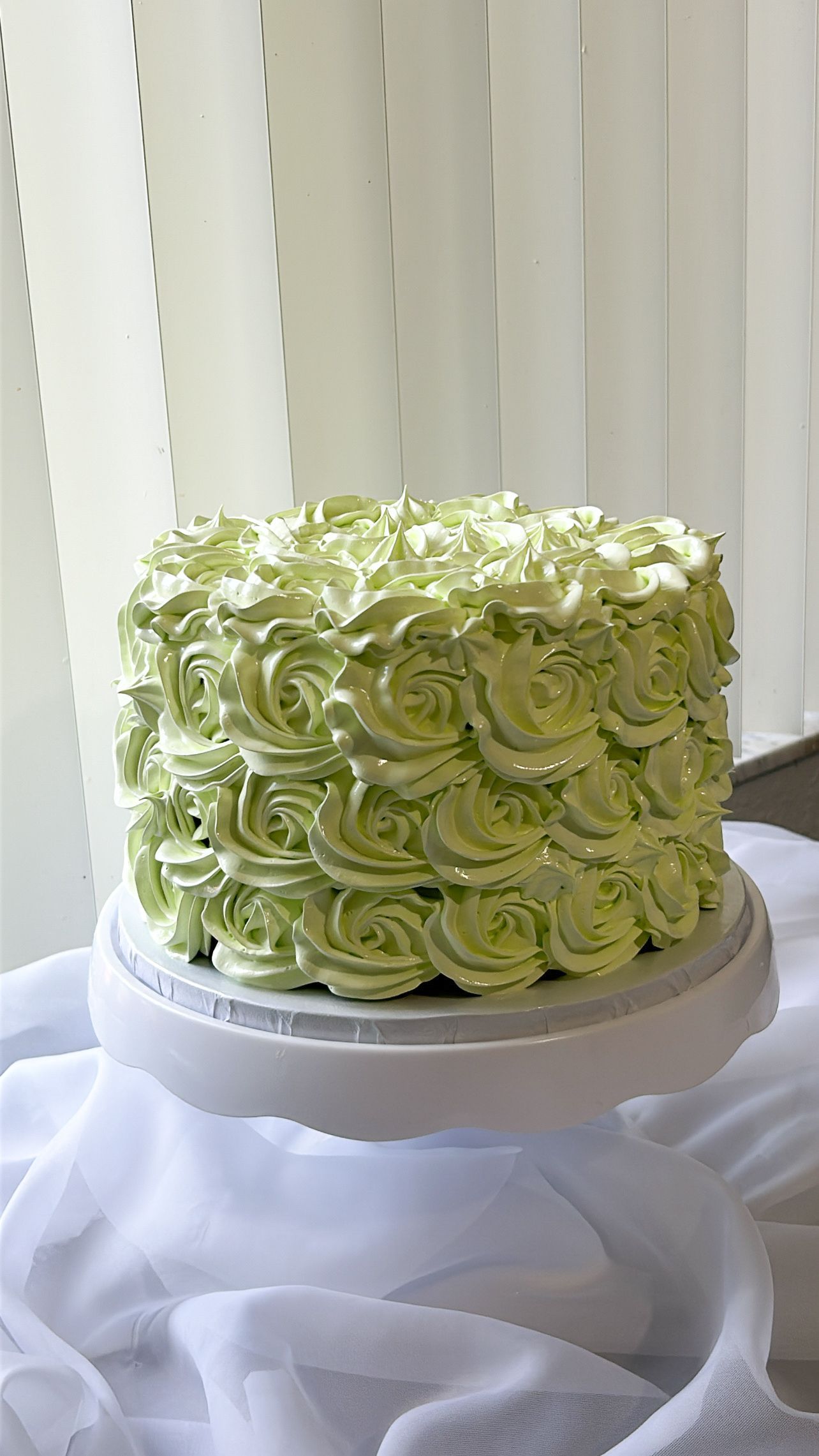 A cake with green frosting is sitting on a white plate on a table.