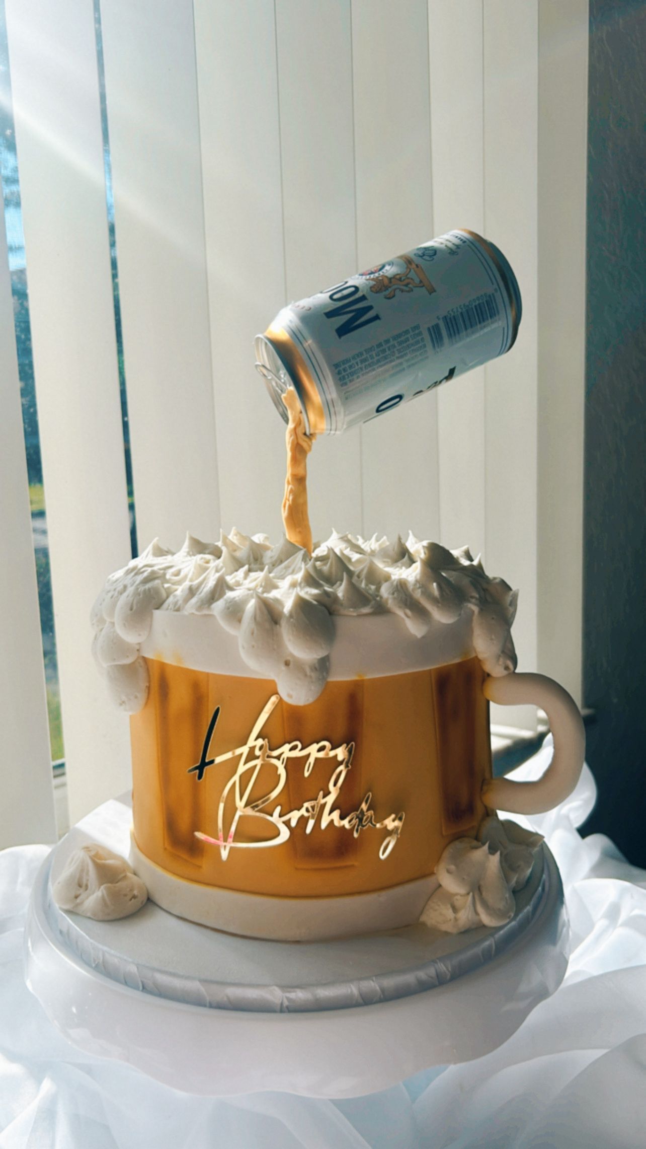 A birthday cake in the shape of a beer mug with a can of beer pouring out of it.