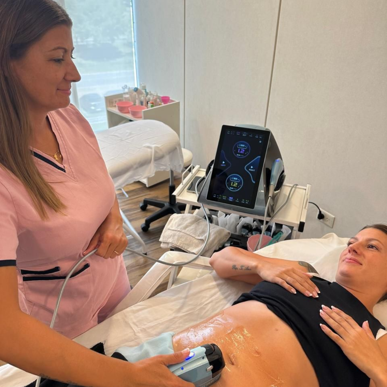 Un profesional realiza un tratamiento láser cosmético en el abdomen de una clienta utilizando equipos especializados.