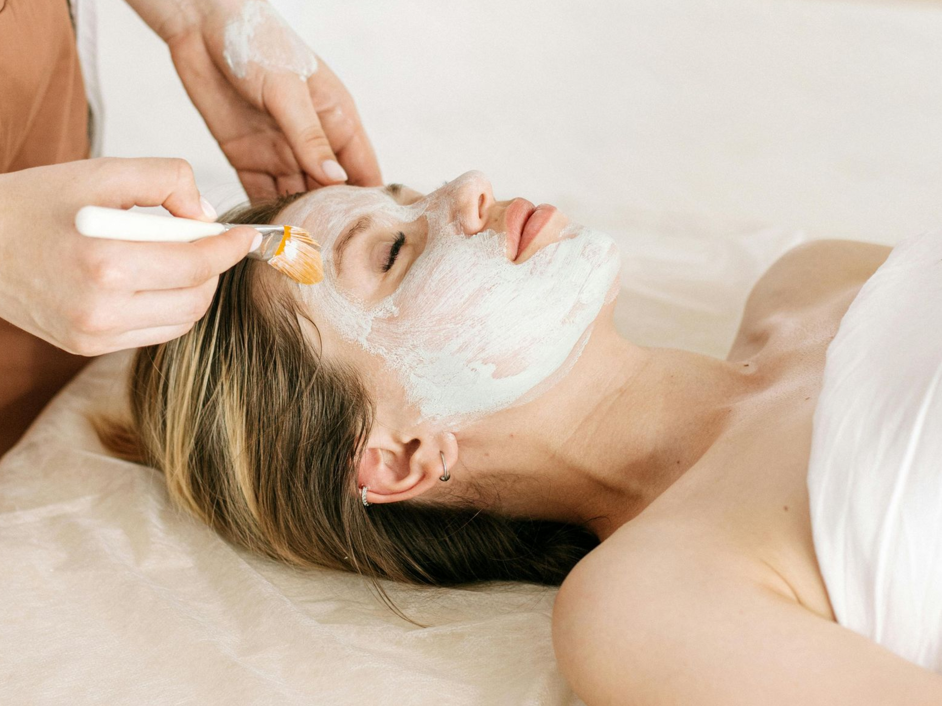 Una persona aplica una mascarilla facial blanca sobre la piel de otra persona