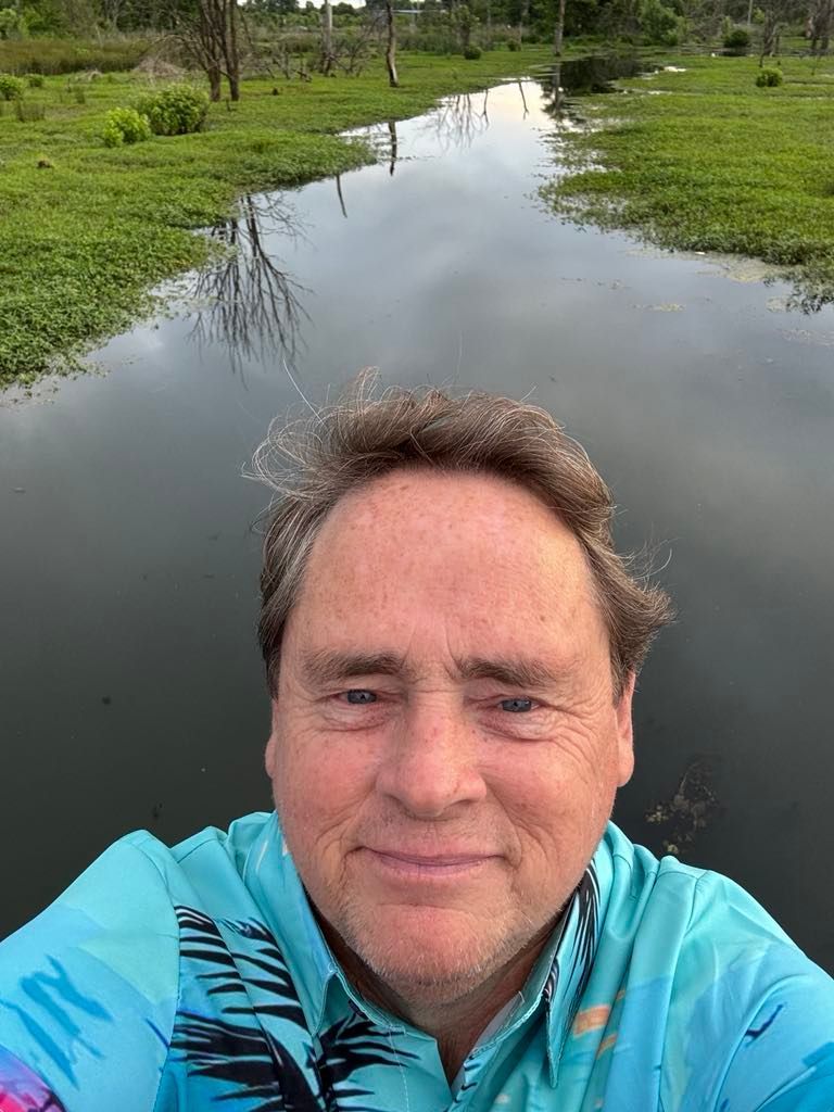 A man is taking a selfie in front of a body of water.