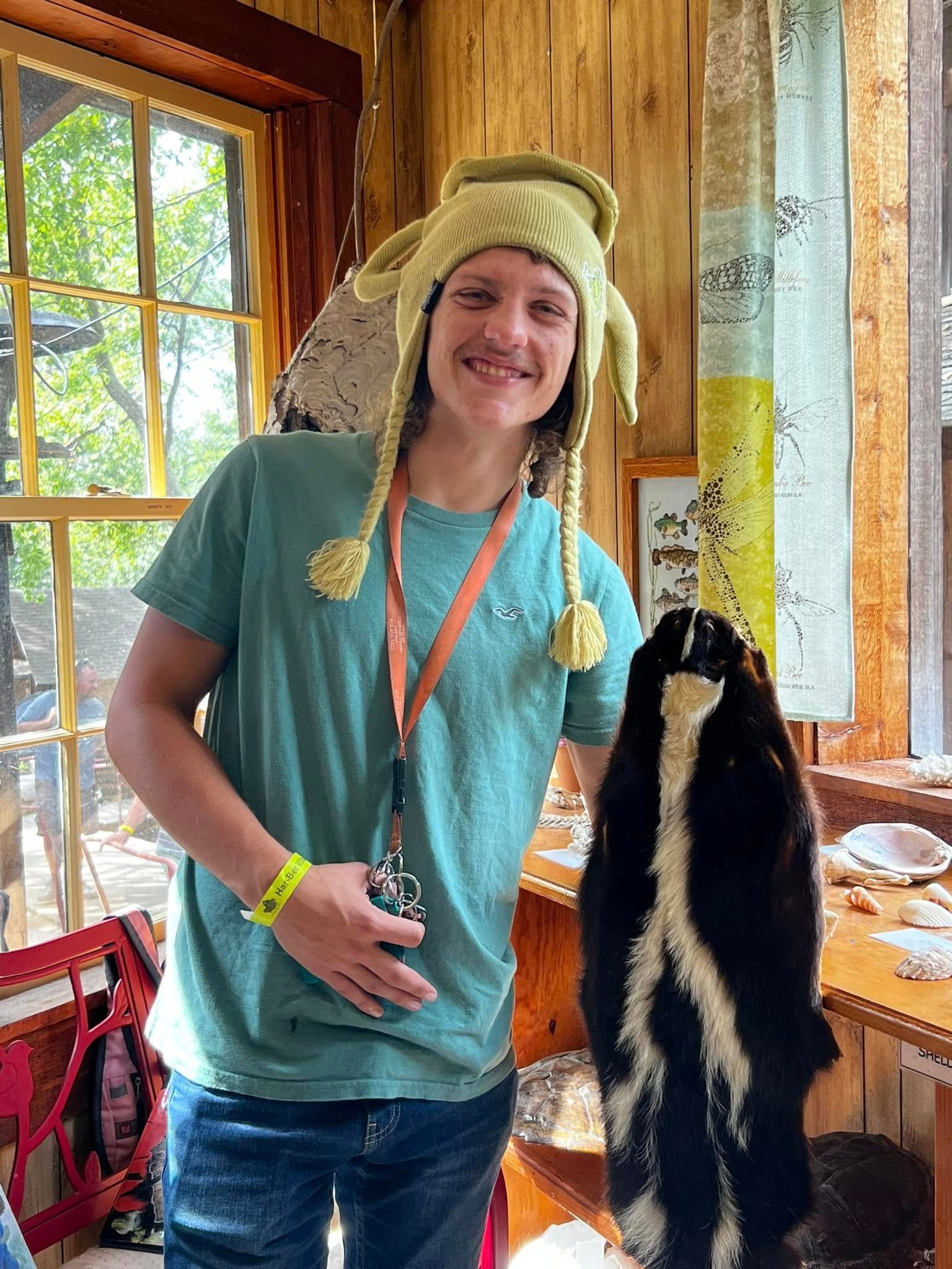 A woman wearing a knitted hat is standing next to a stuffed animal.
