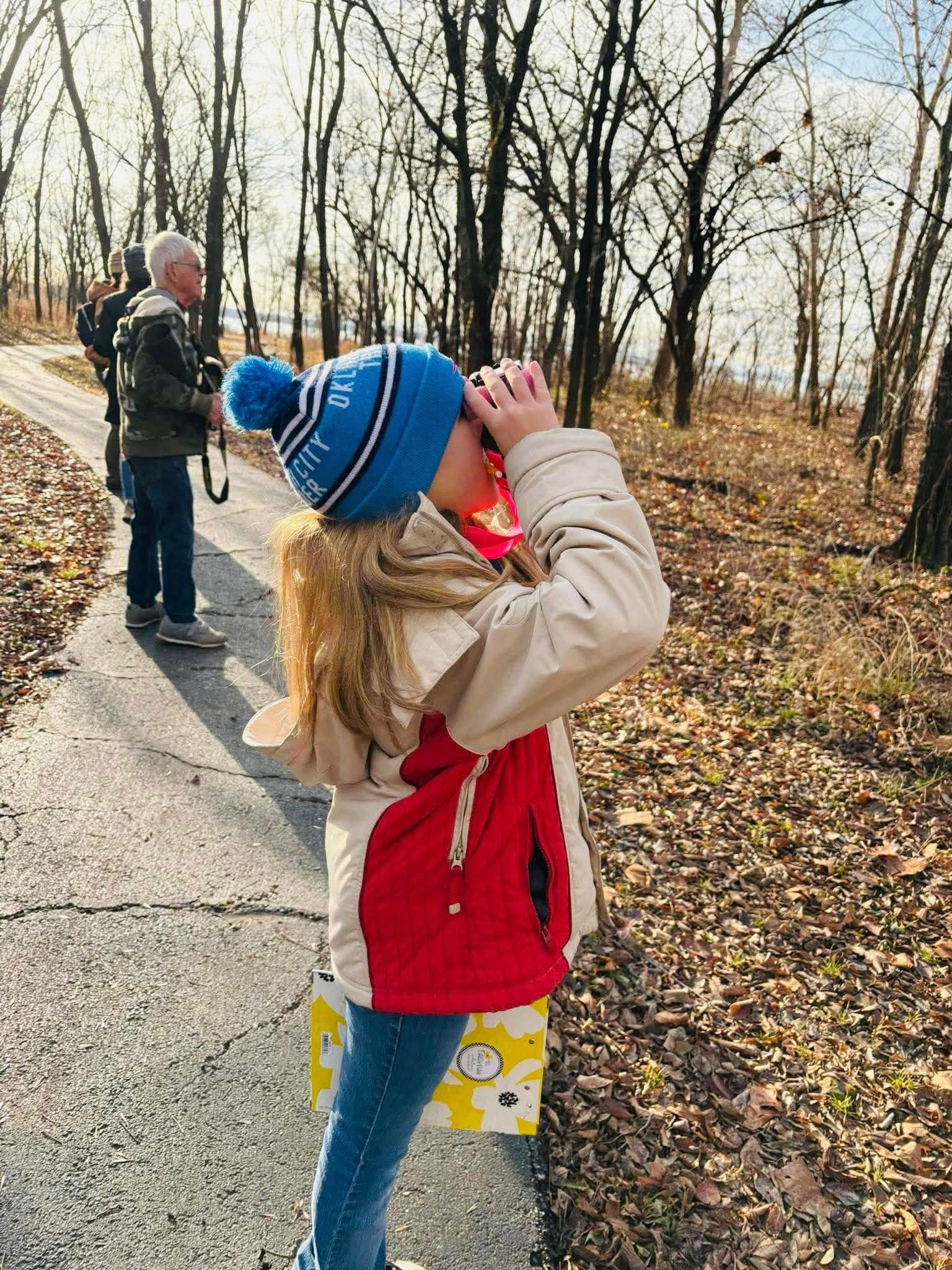 A little girl is looking through binoculars in the woods.
