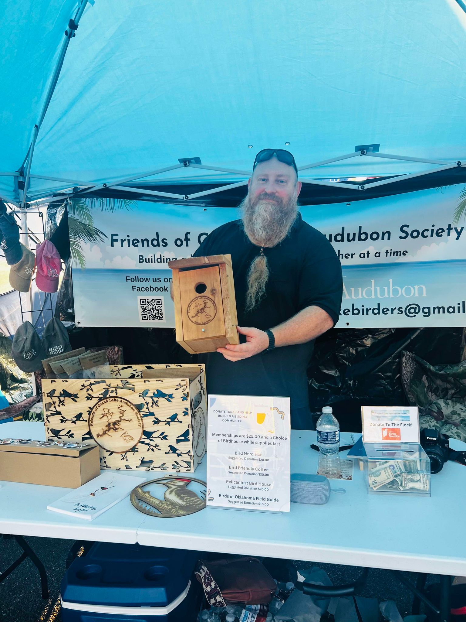 A man with a beard is standing behind a table holding a birdhouse