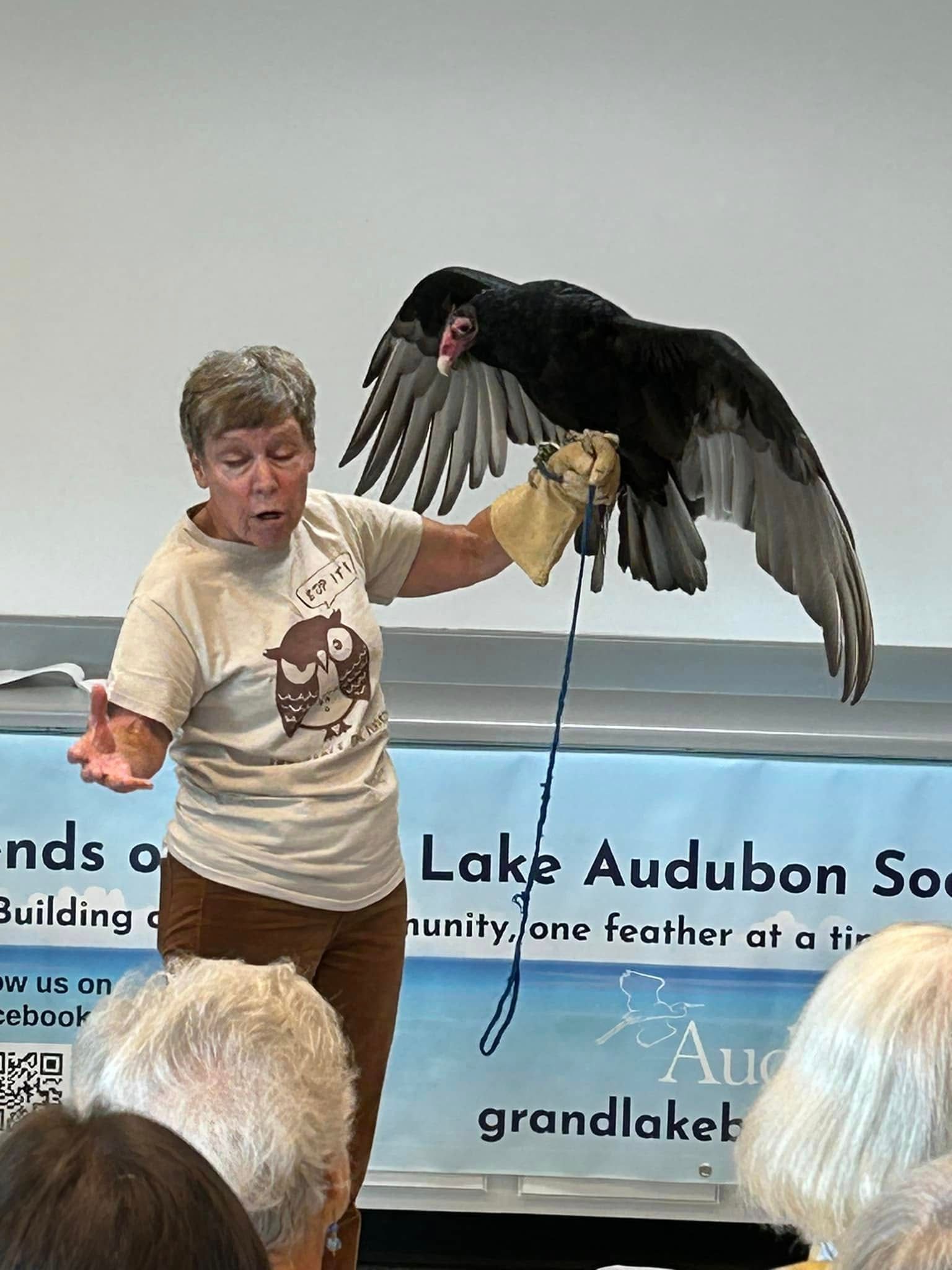 A woman is holding a black bird on a leash in front of a group of people.