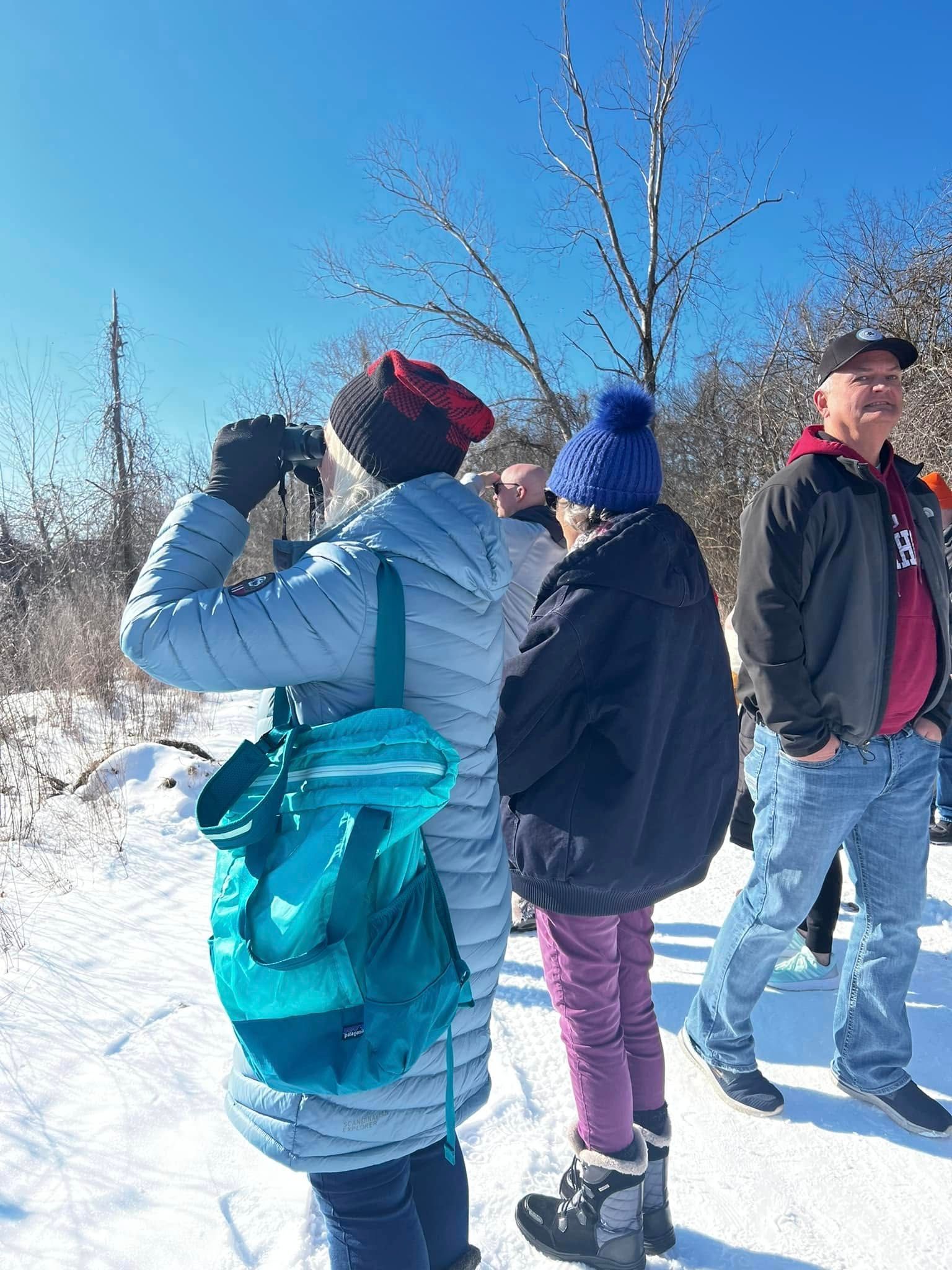 A group of people are standing in the snow looking at birds.