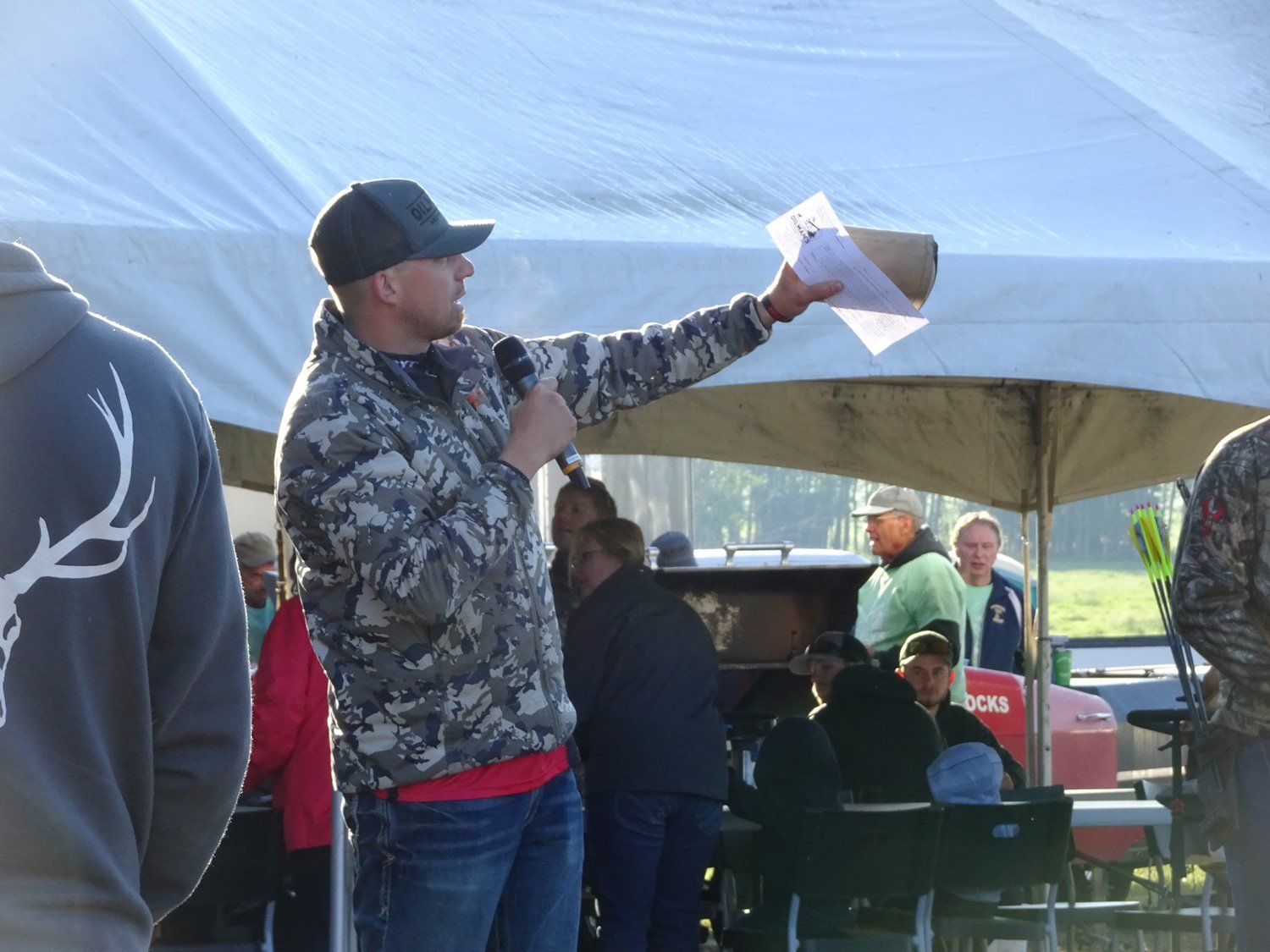 A man in a camo jacket is speaking into a microphone