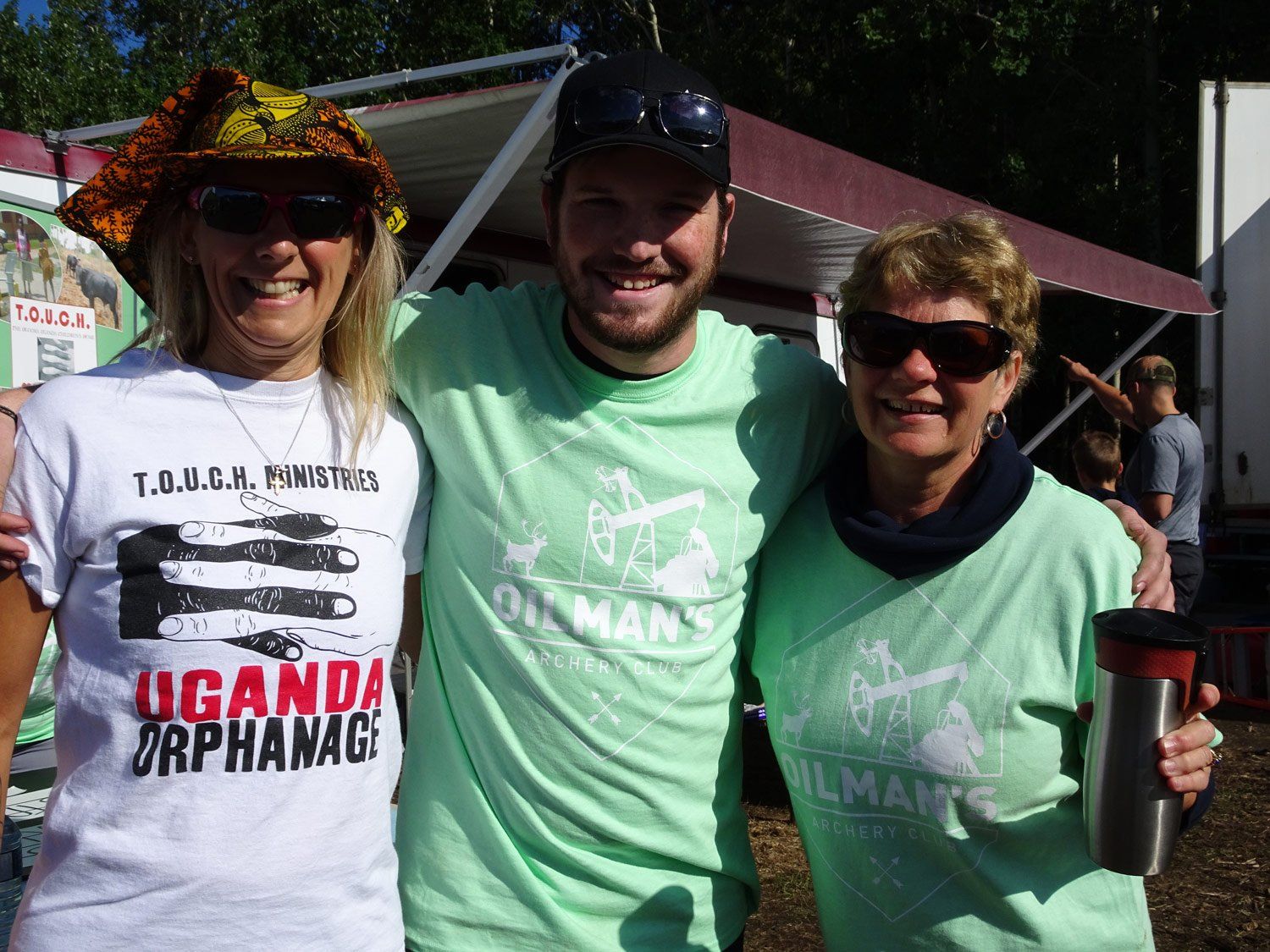 Three people posing for a picture with one wearing a shirt that says uganda orphanage