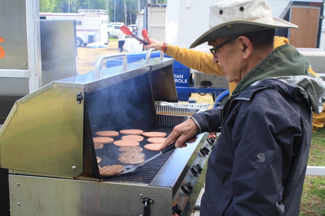 A man in a cowboy hat is cooking hamburgers on a grill.