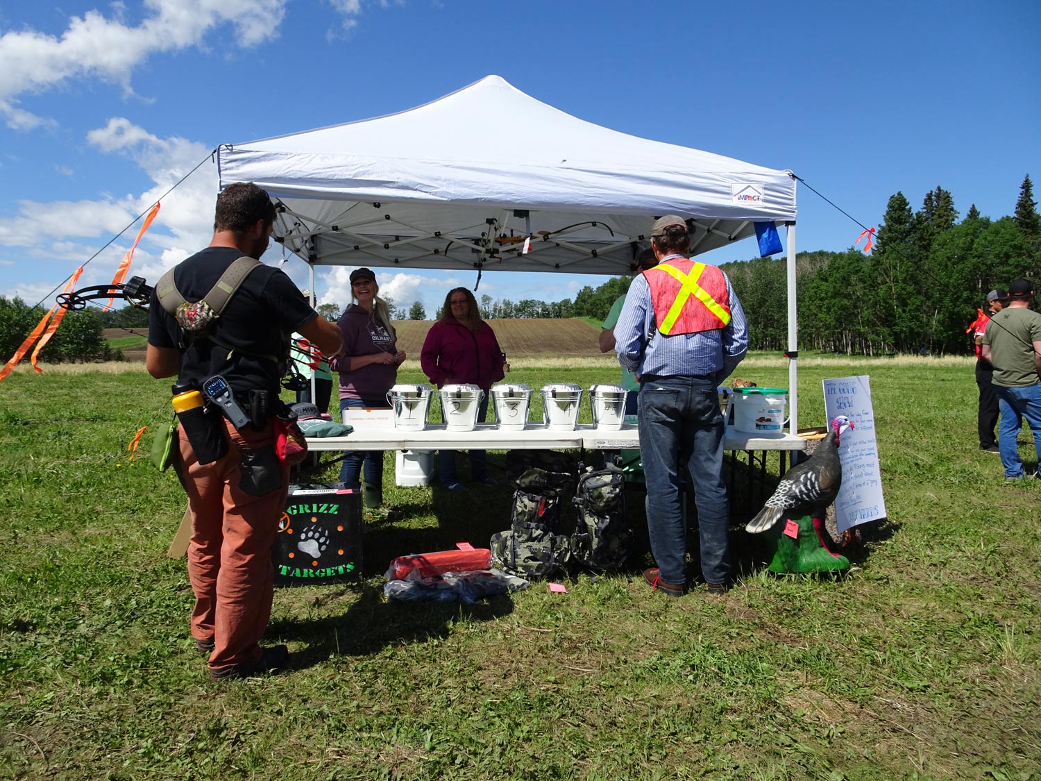 A group of people are standing under a white tent in a field.
