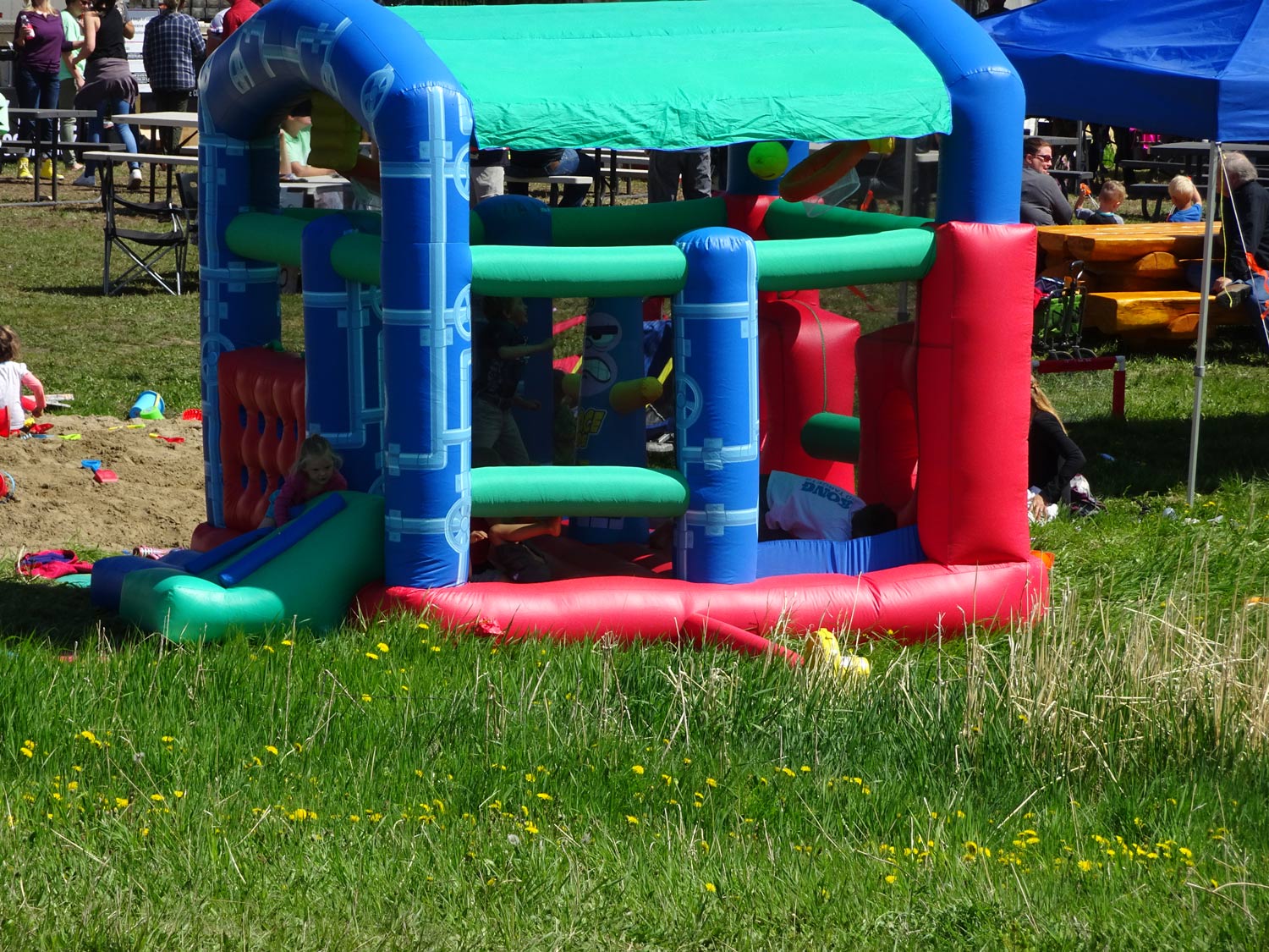 A red and blue bouncy house is sitting in the middle of a grassy field.