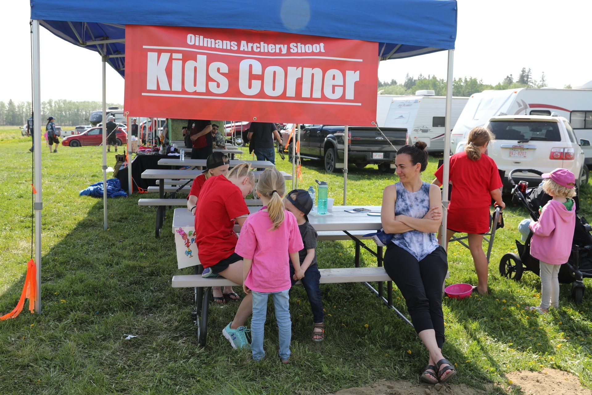 A group of people are sitting under a tent that says kids corner