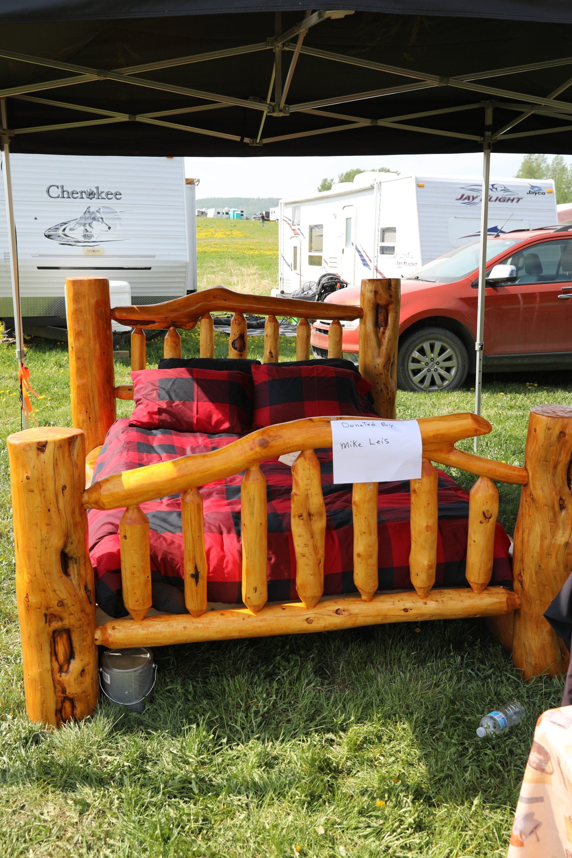 A log bed is sitting in the grass under a tent.