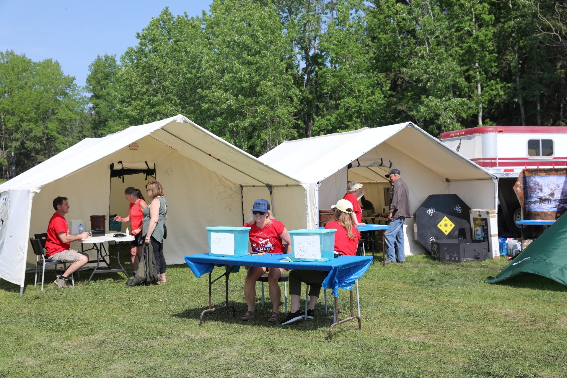 A group of people are sitting at tables under tents in a field.