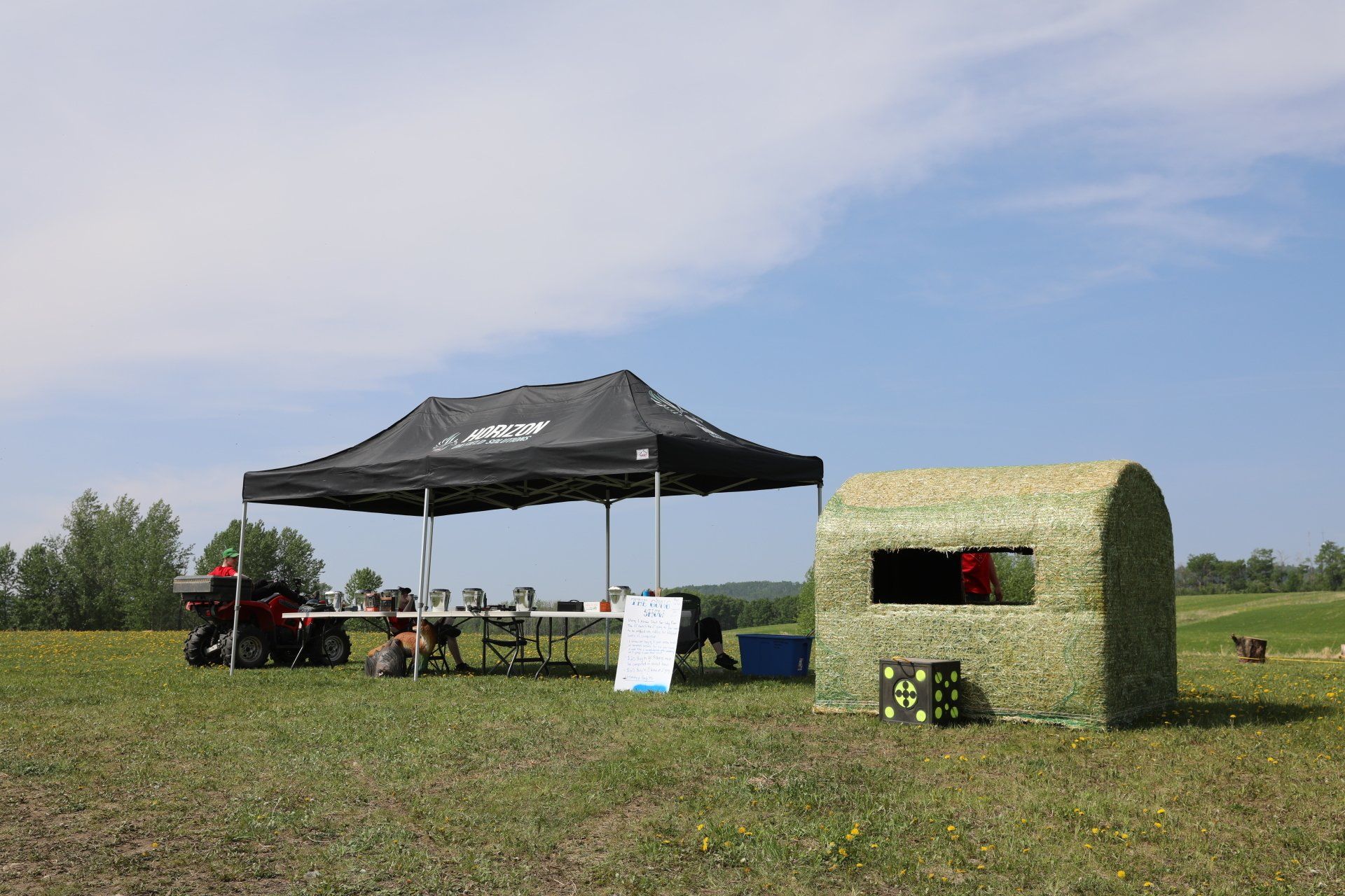A group of people are sitting under a tent in a field.