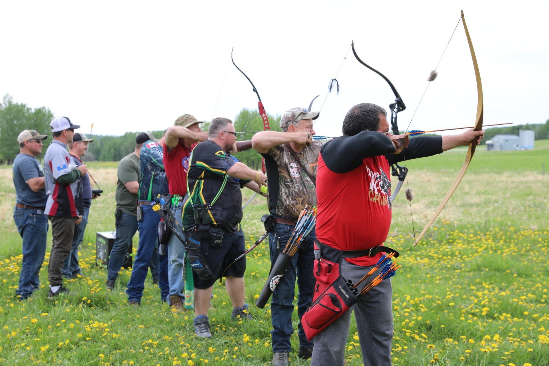 A group of men are standing in a field holding bows and arrows.