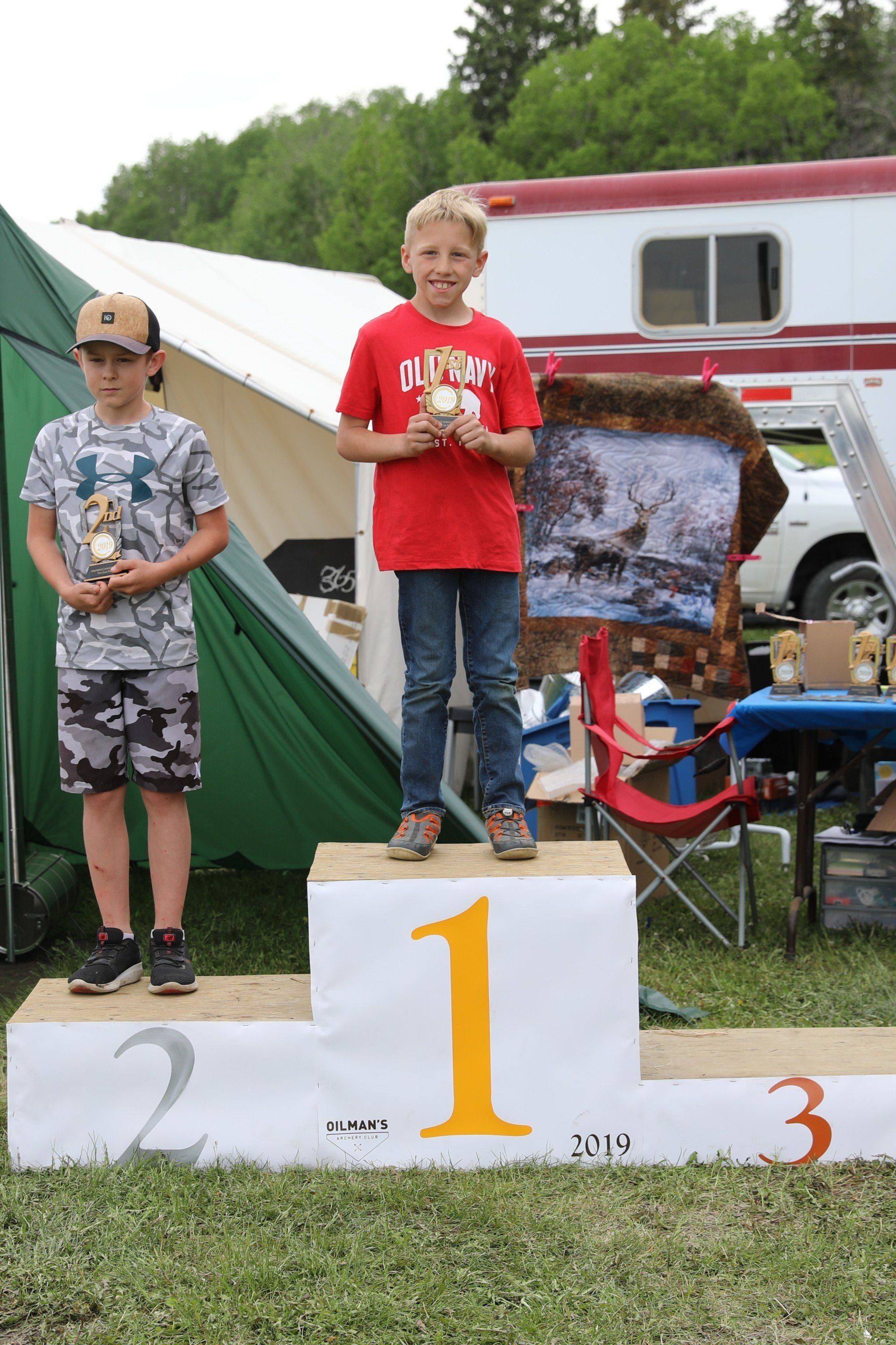 Two young boys are standing on a podium holding trophies.