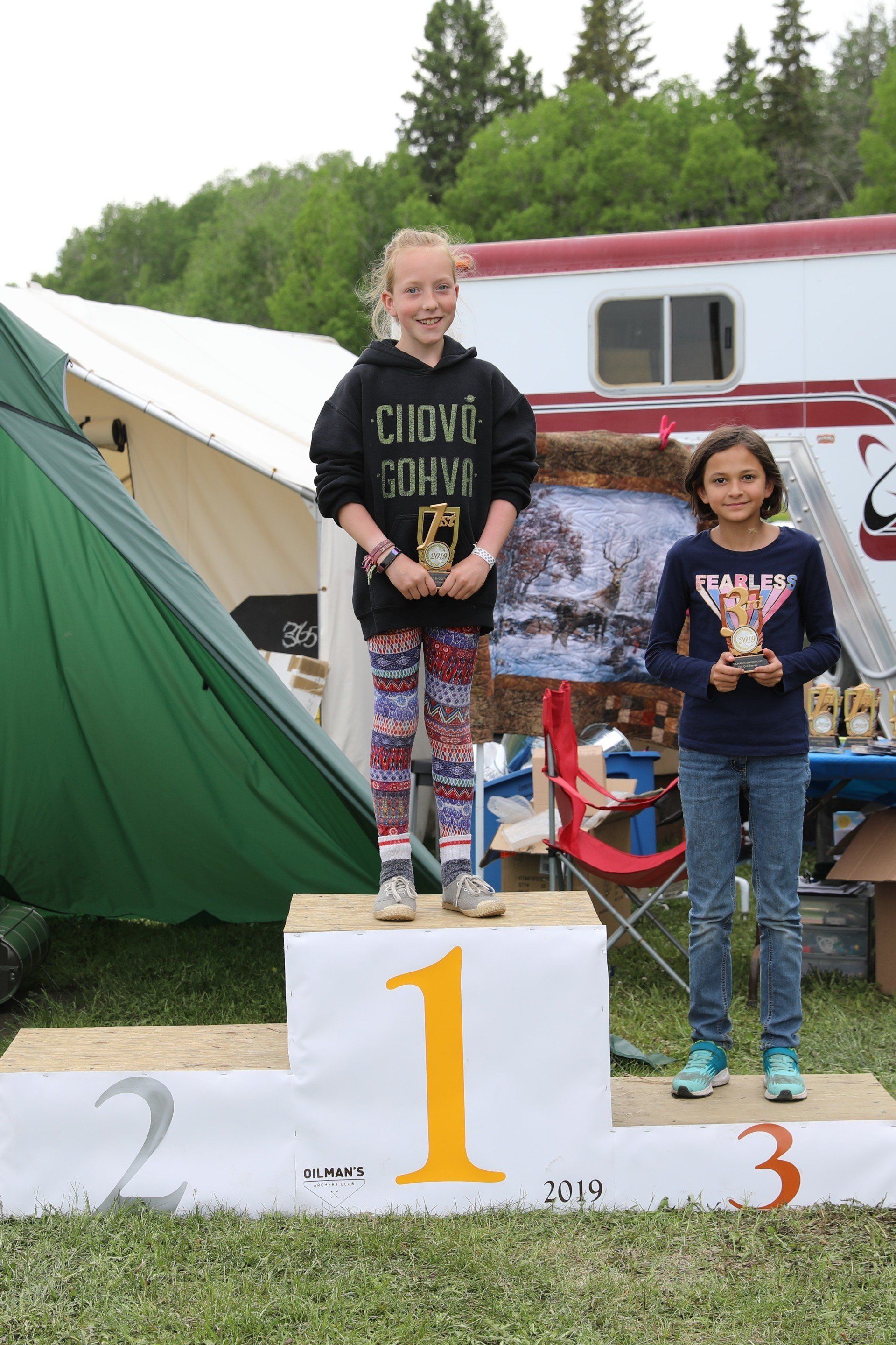 Two young girls are standing on a podium holding trophies.