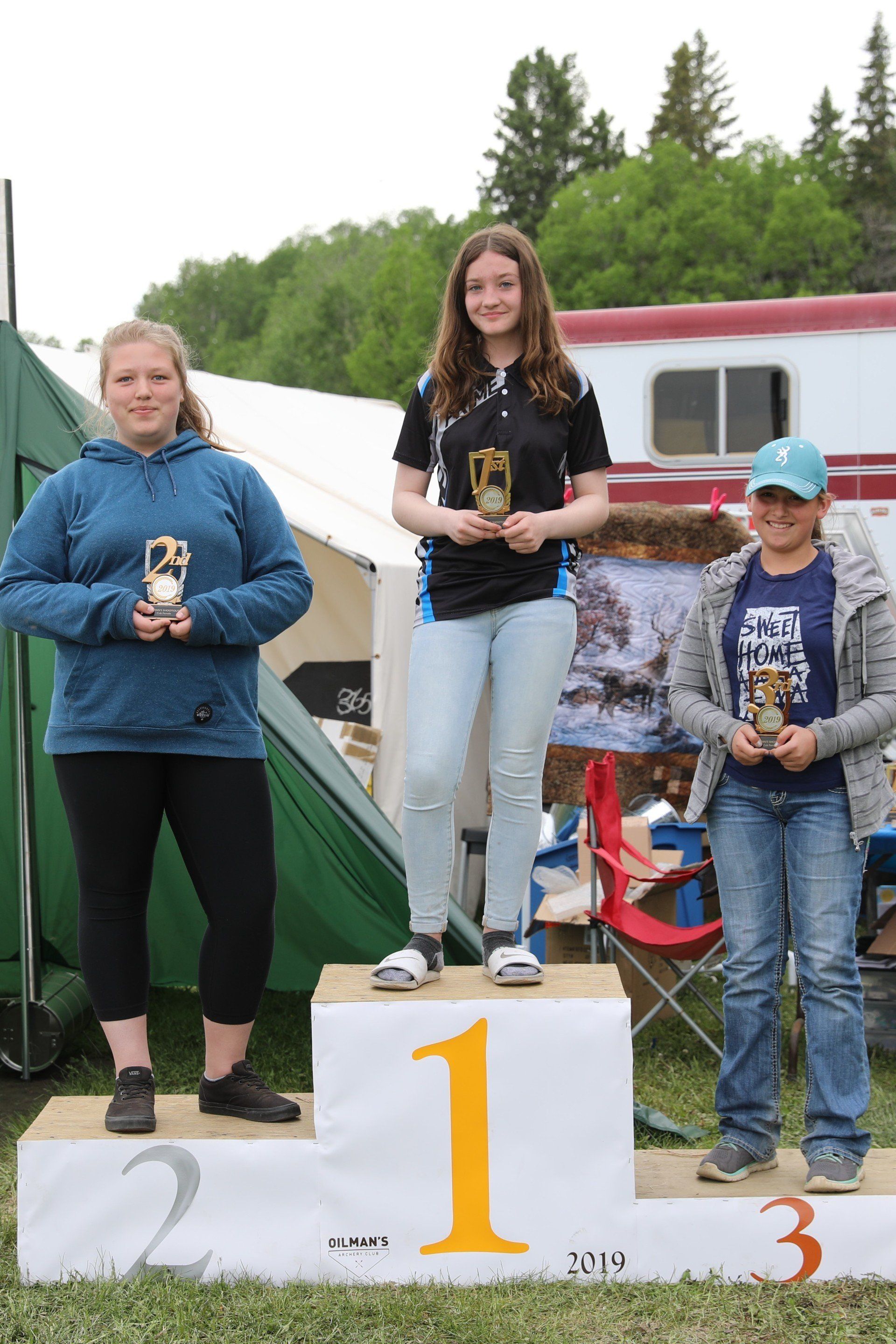 Three women are standing on a podium holding trophies.