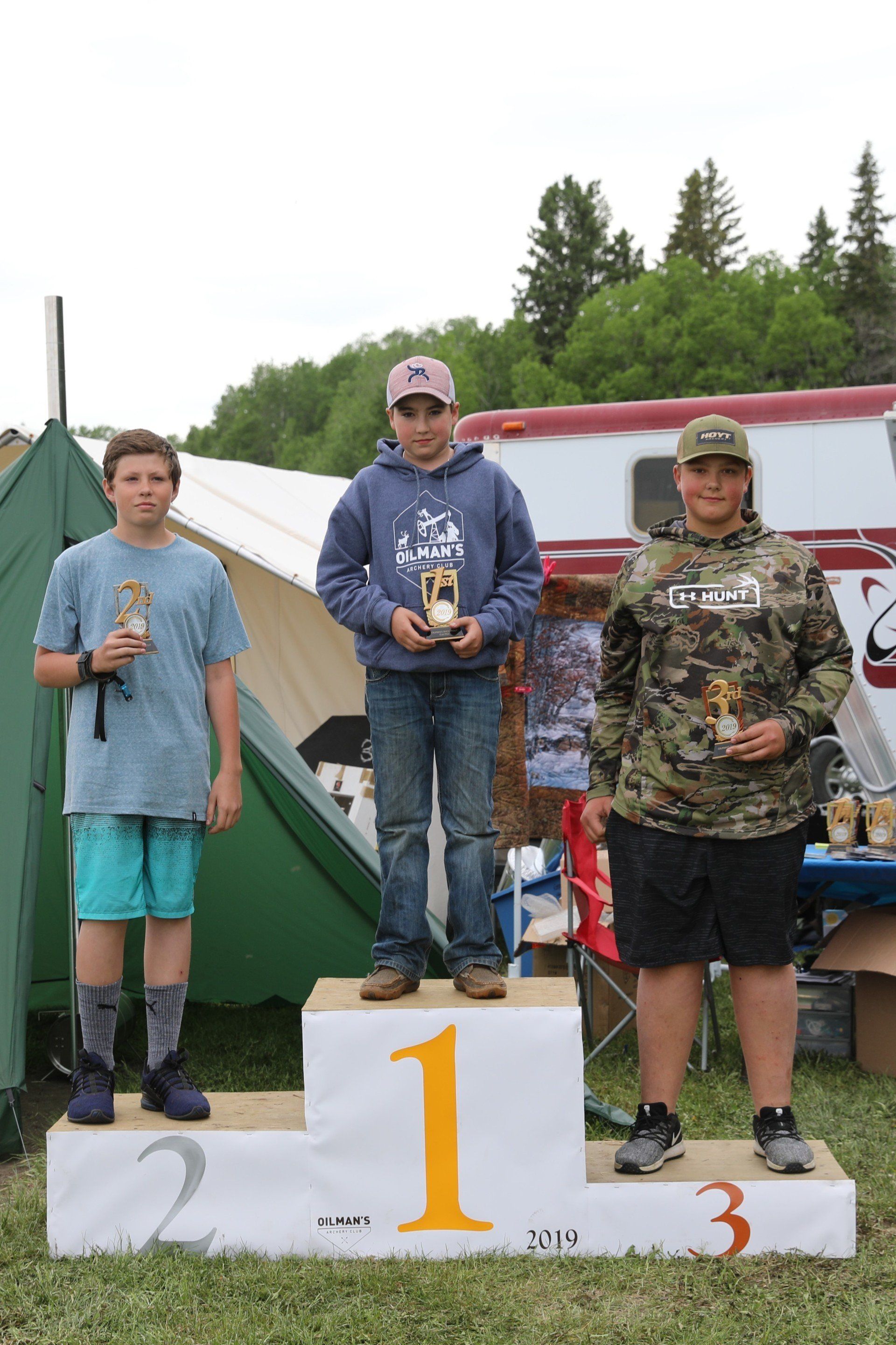 Three young men are standing on a podium holding trophies.