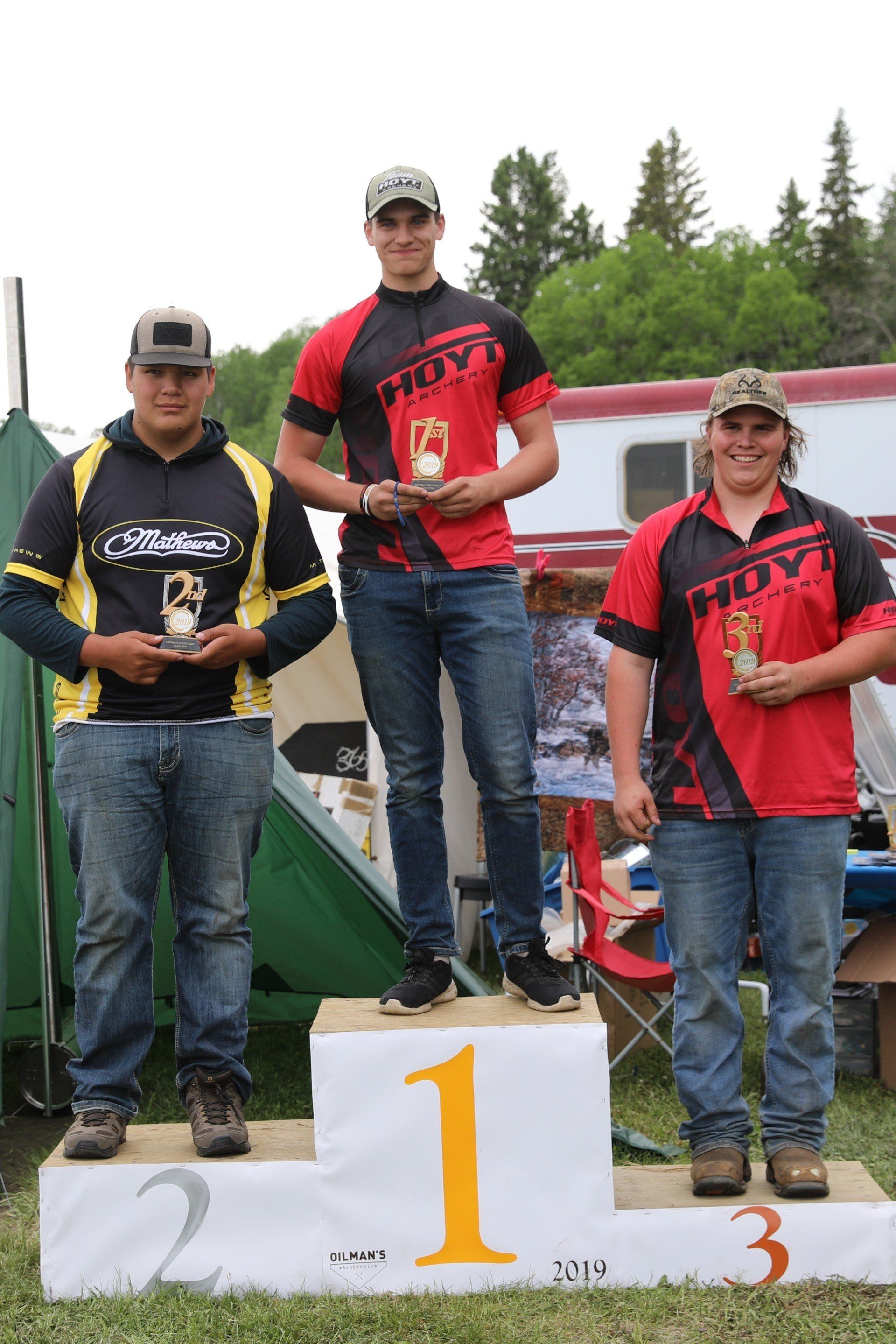 Three men are standing on a podium holding trophies.