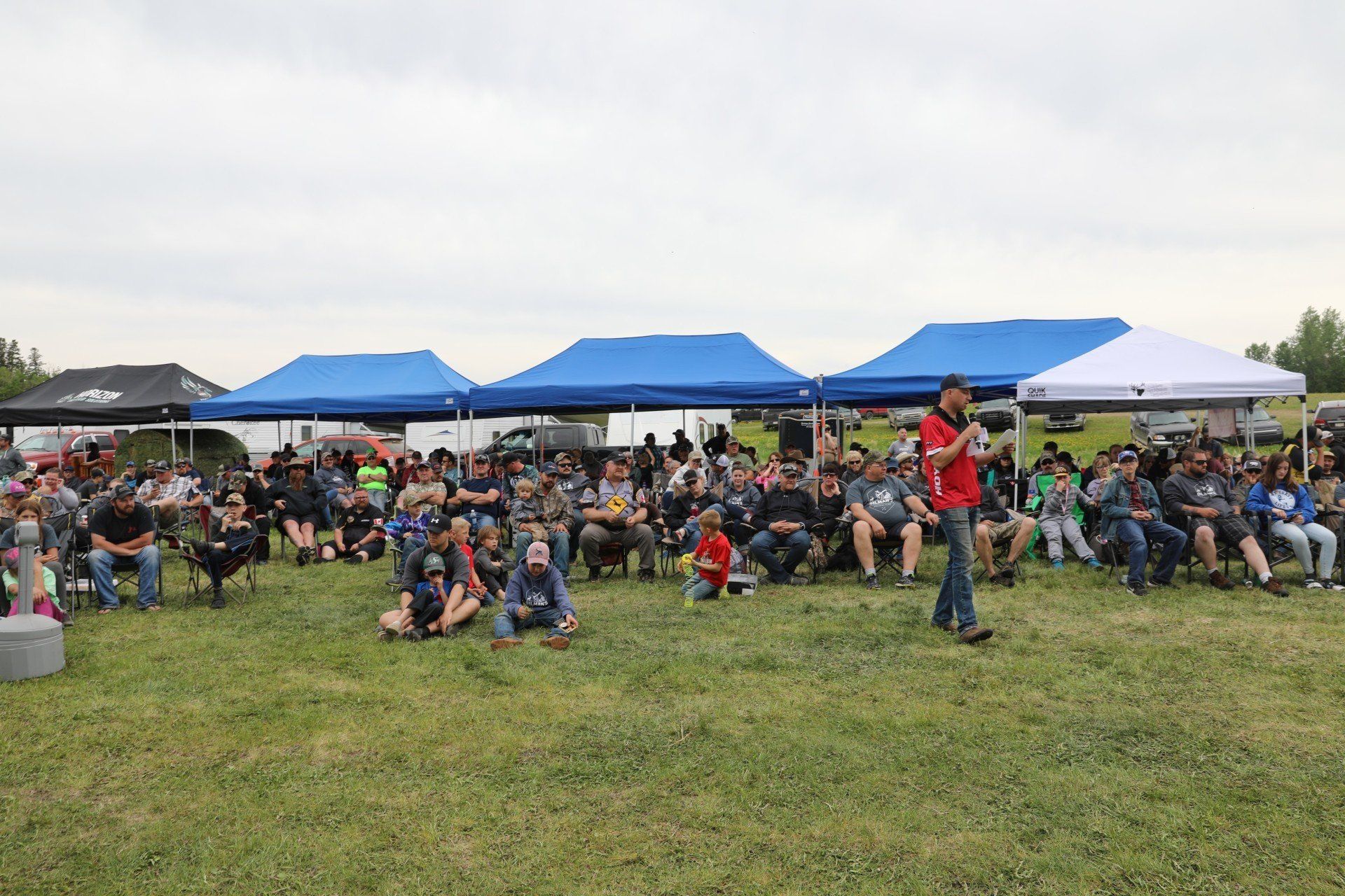 A group of people are sitting under tents in a field.