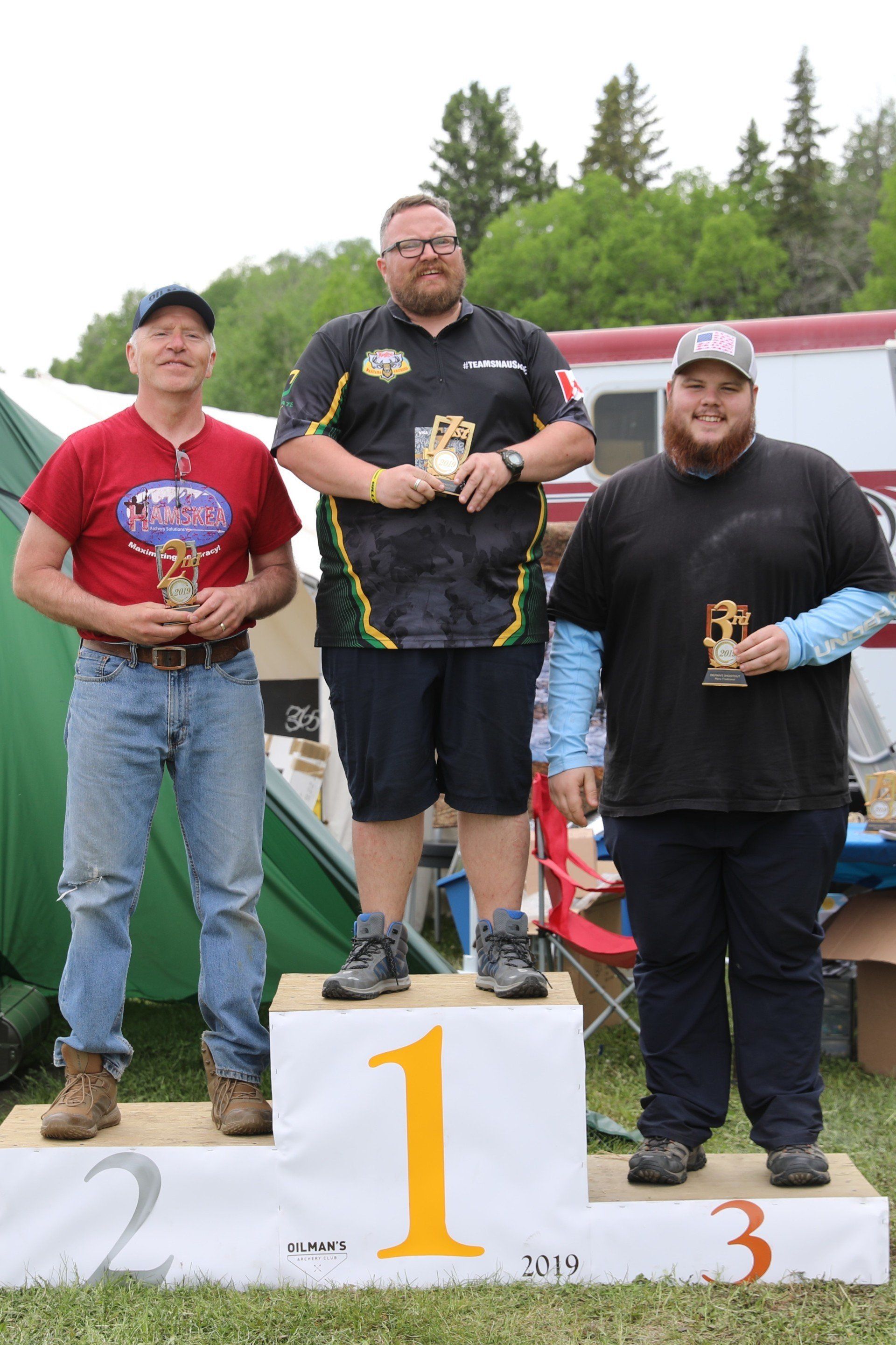 Three men are standing on a podium holding trophies.