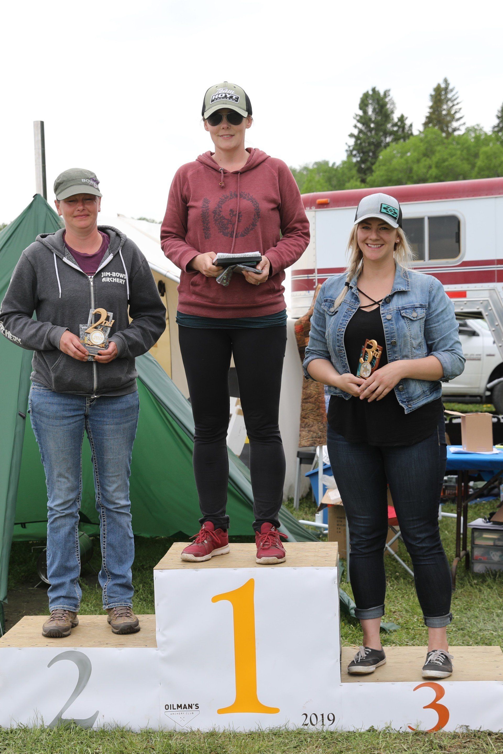 Three women are standing on a podium holding trophies.
