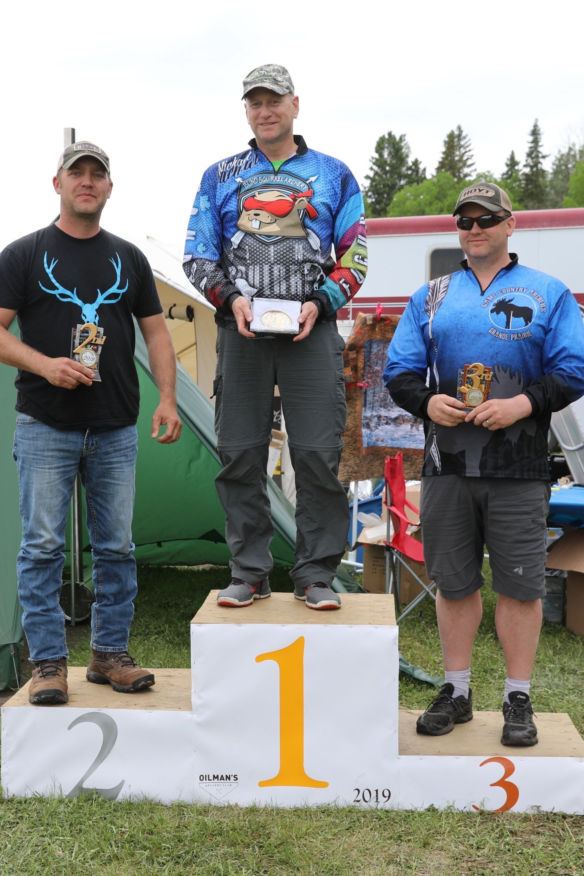 Three men are standing on a podium holding trophies.