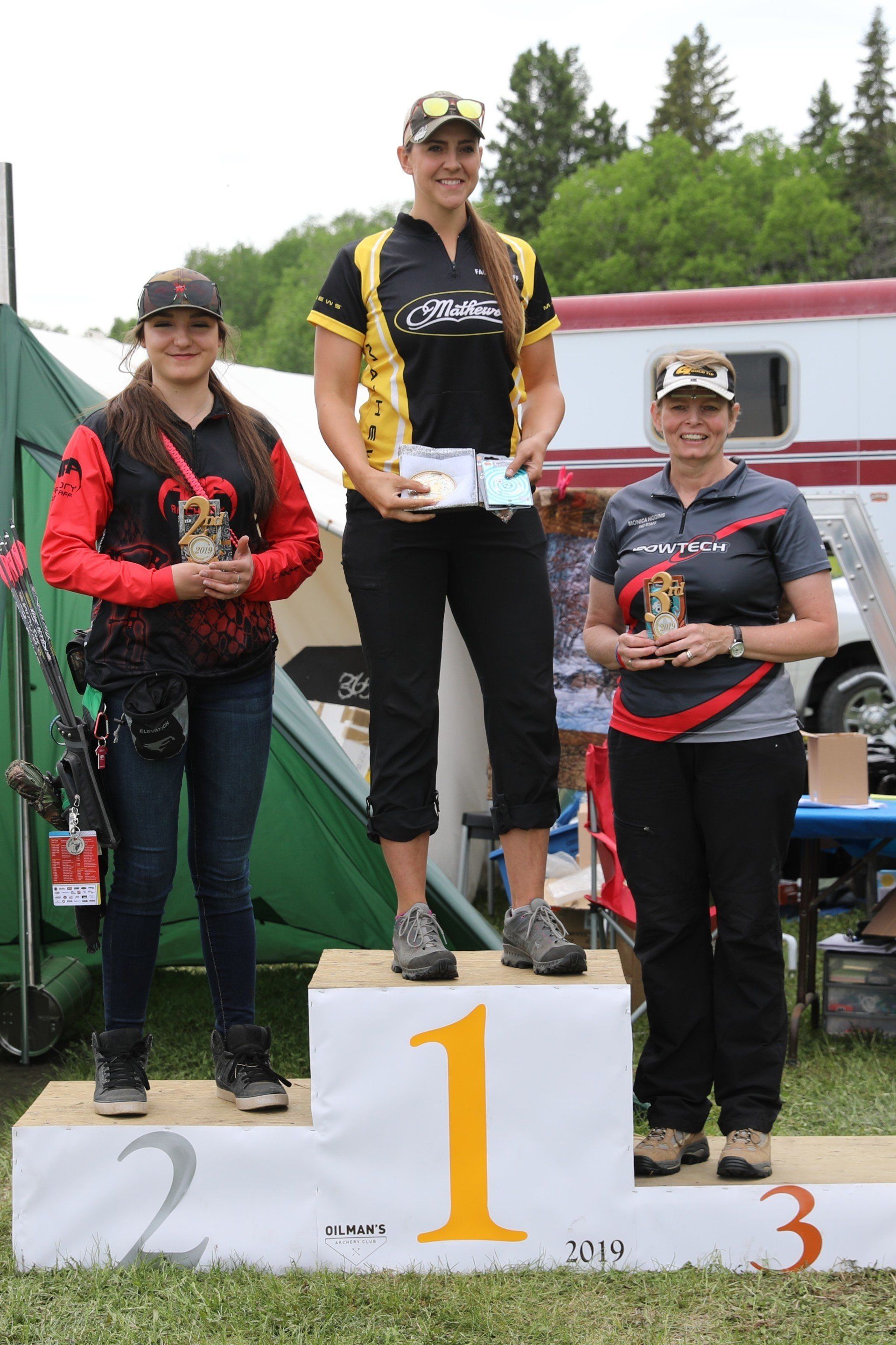 Three women are standing on a podium holding trophies.