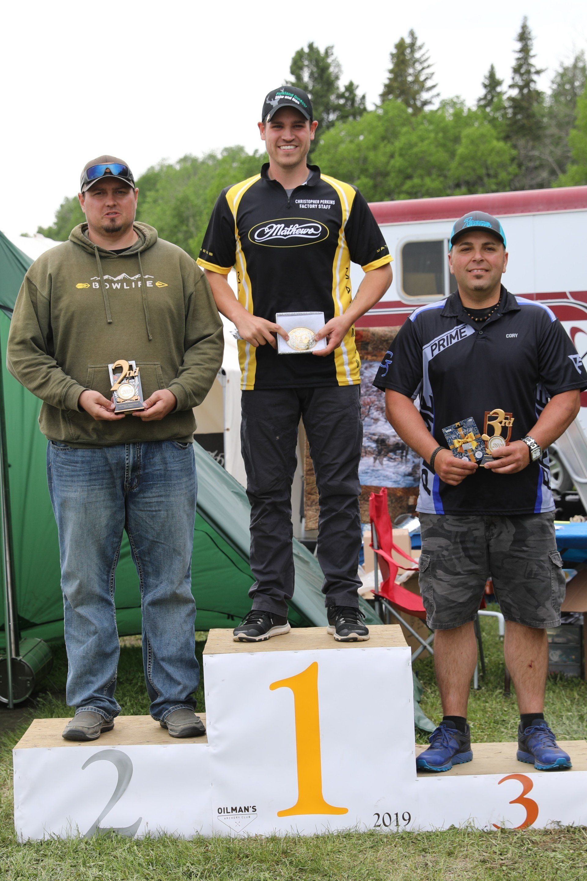 Three men are standing on a podium holding trophies.