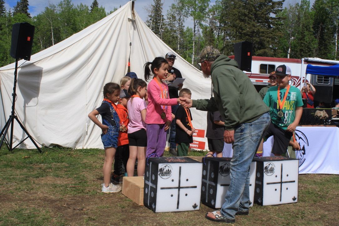 A man is shaking hands with a group of children in front of a tent.