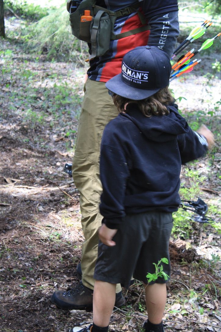 A man and a boy are standing in the woods holding bows and arrows.