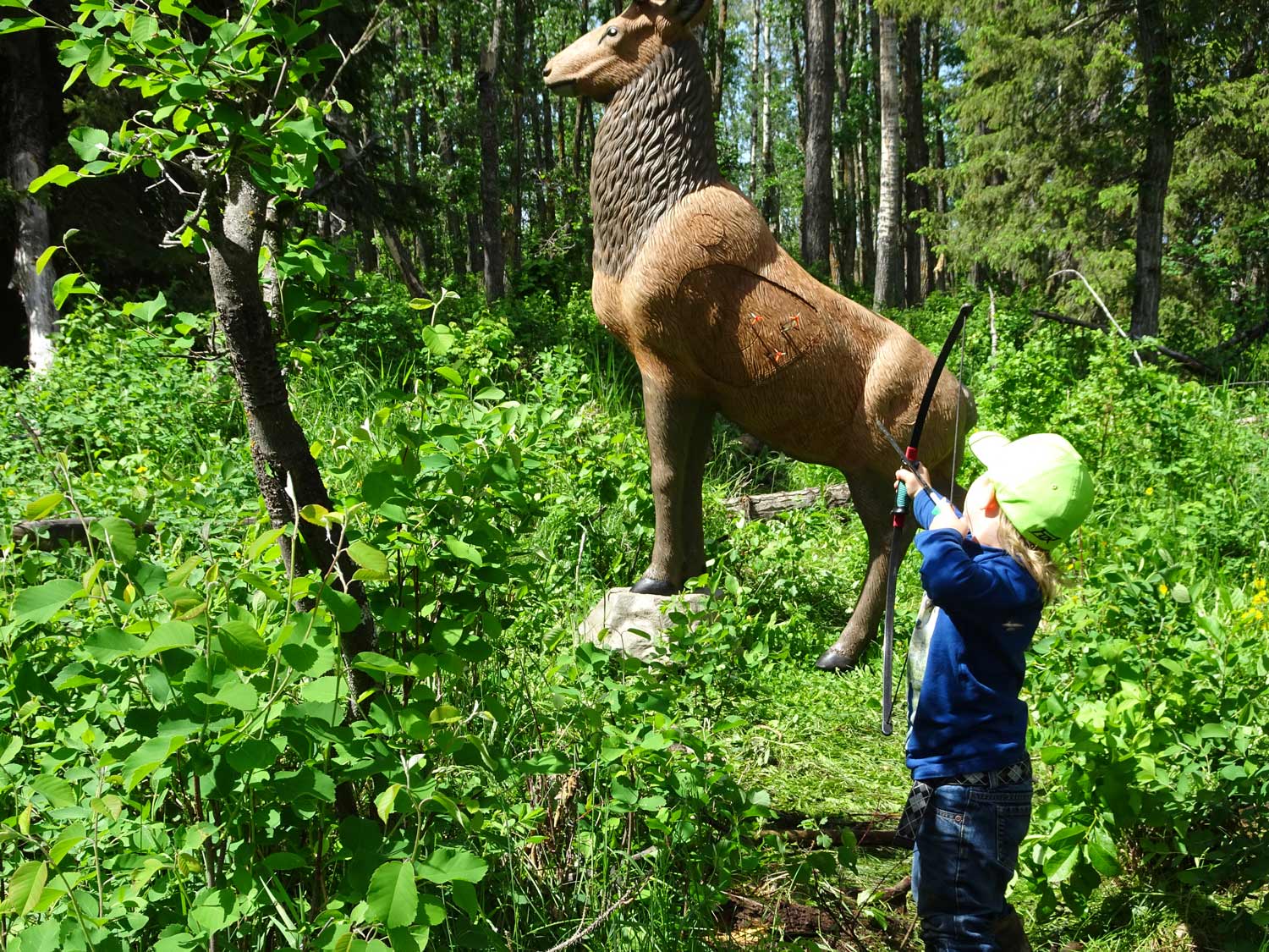 A child is standing next to a statue of a deer in the woods.