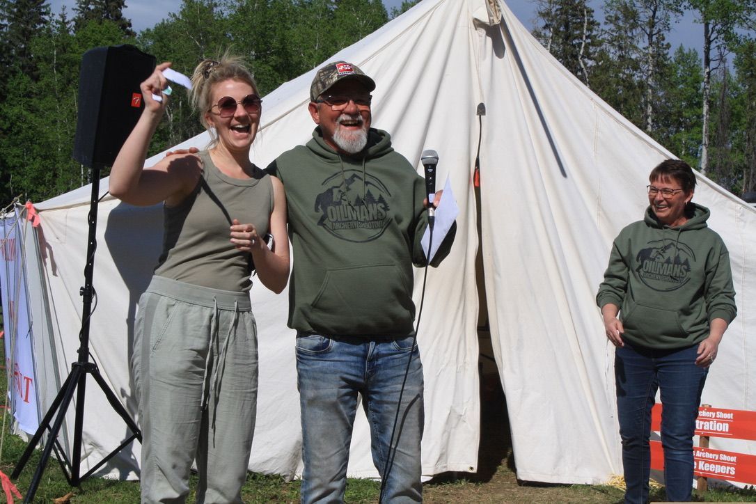 A man is holding a microphone while standing next to a woman in front of a tent.