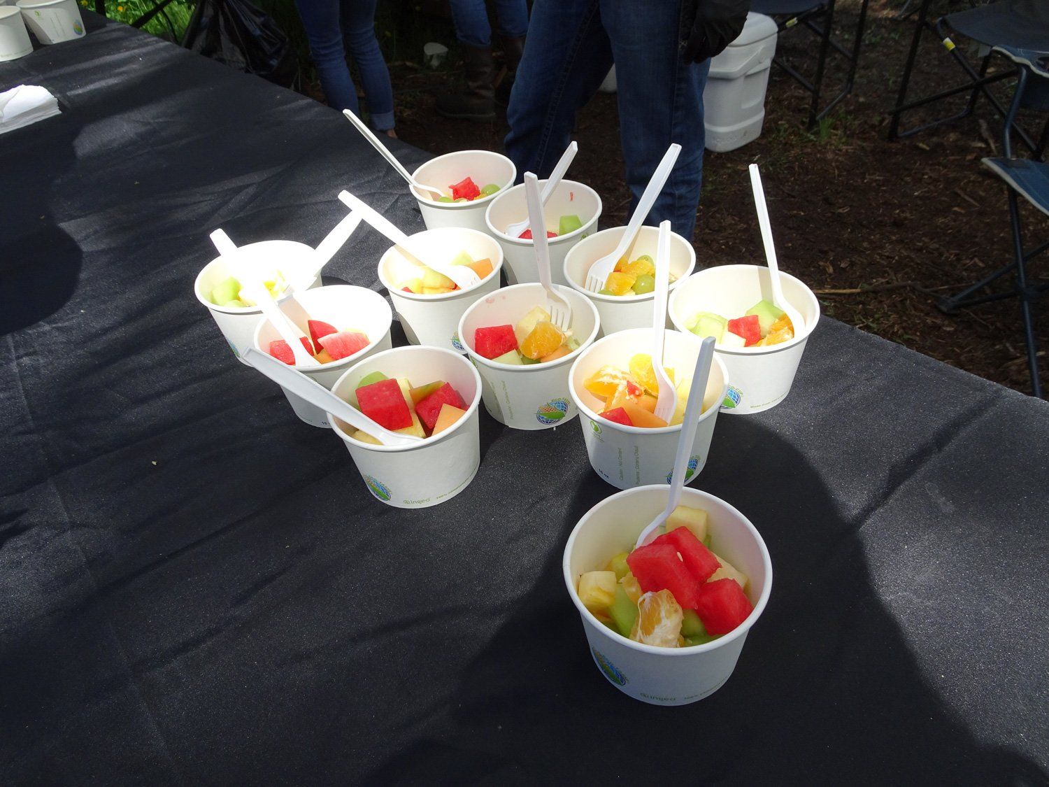 A bunch of cups filled with fruit and spoons on a table