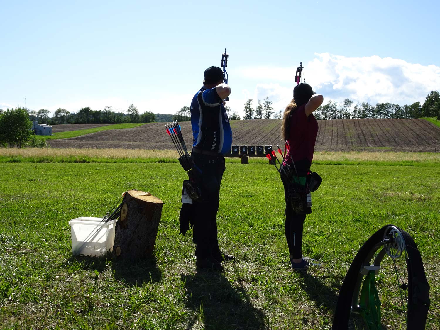 A man and a woman are standing in a field holding bows and arrows.