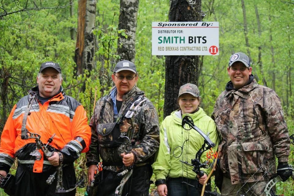 A group of people standing next to each other in the woods holding bows and arrows.