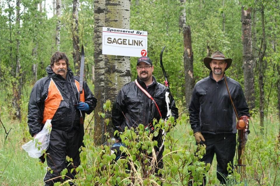 Three men are standing in a forest with a sign that says sagelink.