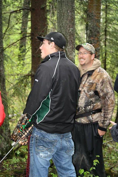 Two men are standing in the woods holding bows and arrows.
