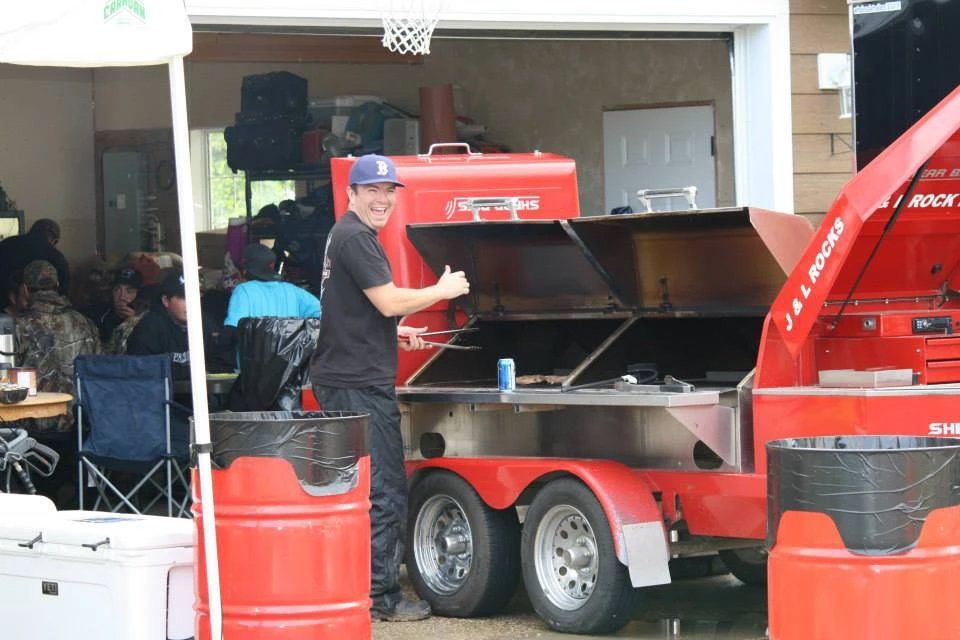 A man is standing in front of a red trailer with the hood open.