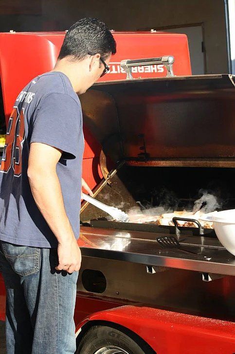A man in a blue shirt is standing in front of a sherpa grill