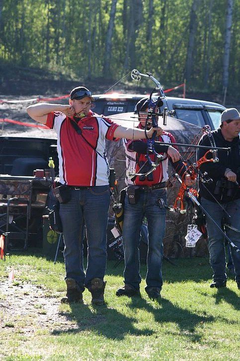 A group of men are standing in a field holding bows and arrows.